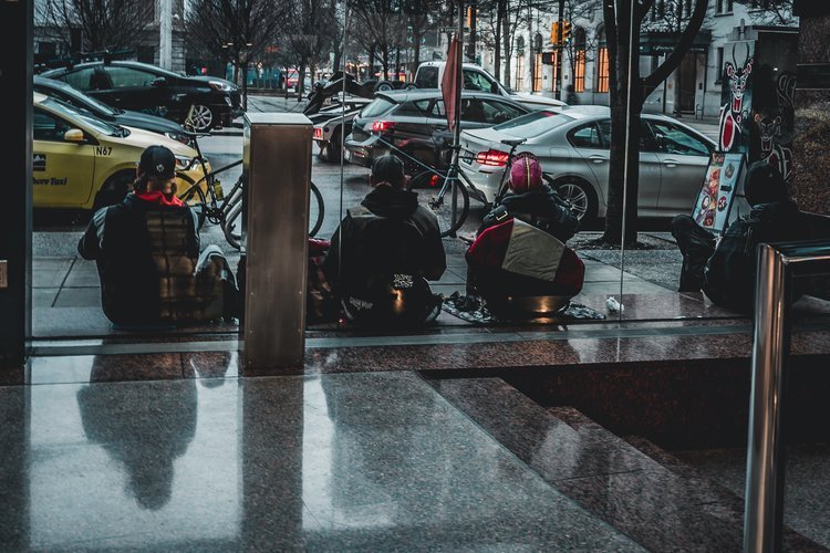 People sitting on the ground inside a glass-walled building, with bikes and cars outside on the street.