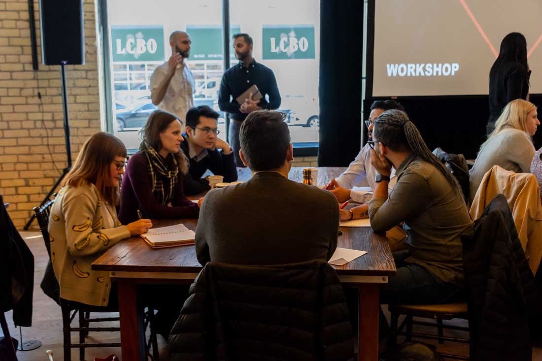 Group of people sitting and standing in a workshop setting, discussing and taking notes.