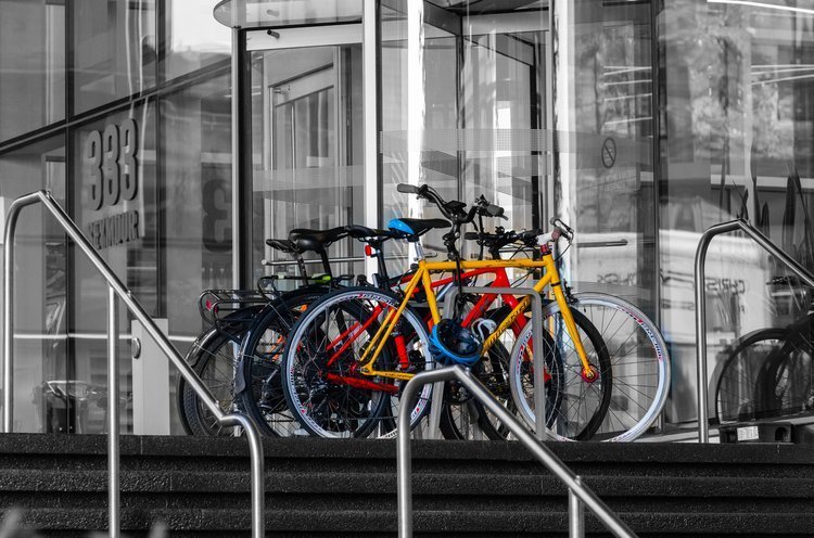 Several colorful bicycles parked outside a building entrance with glass doors.