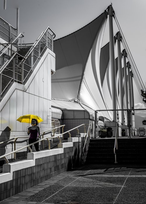 Person holding yellow umbrella near modern architectural structure with large white sails.