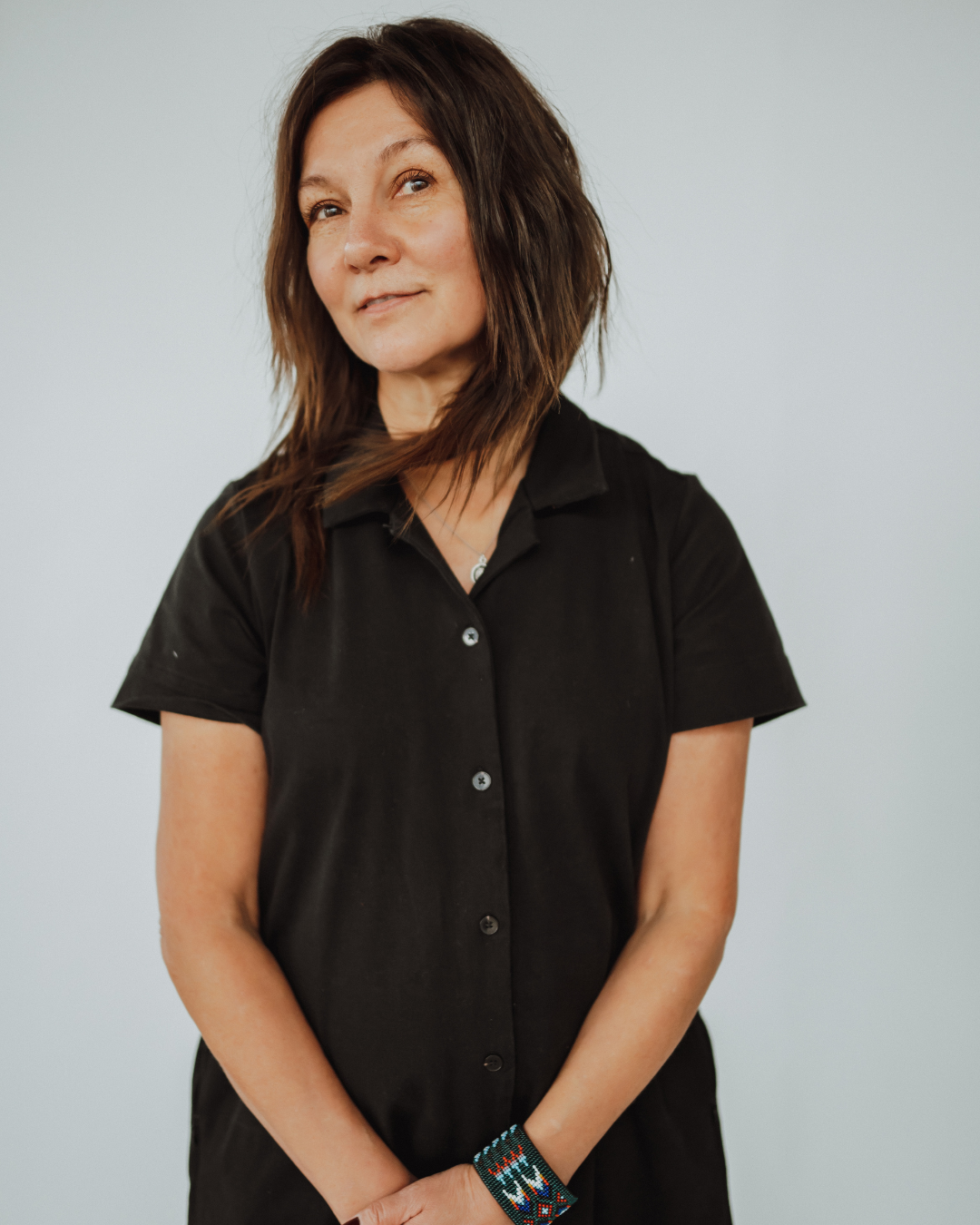 Woman standing in a salon, resting against a styling chair, wearing a black sweater, blue jeans, and black boots. Mirrors and clothing racks are in the background.