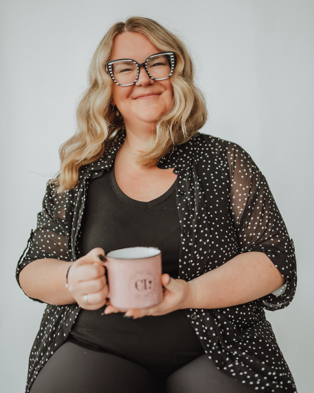Smiling person sitting in a hair salon, wearing floral kimono and large eyeglasses.