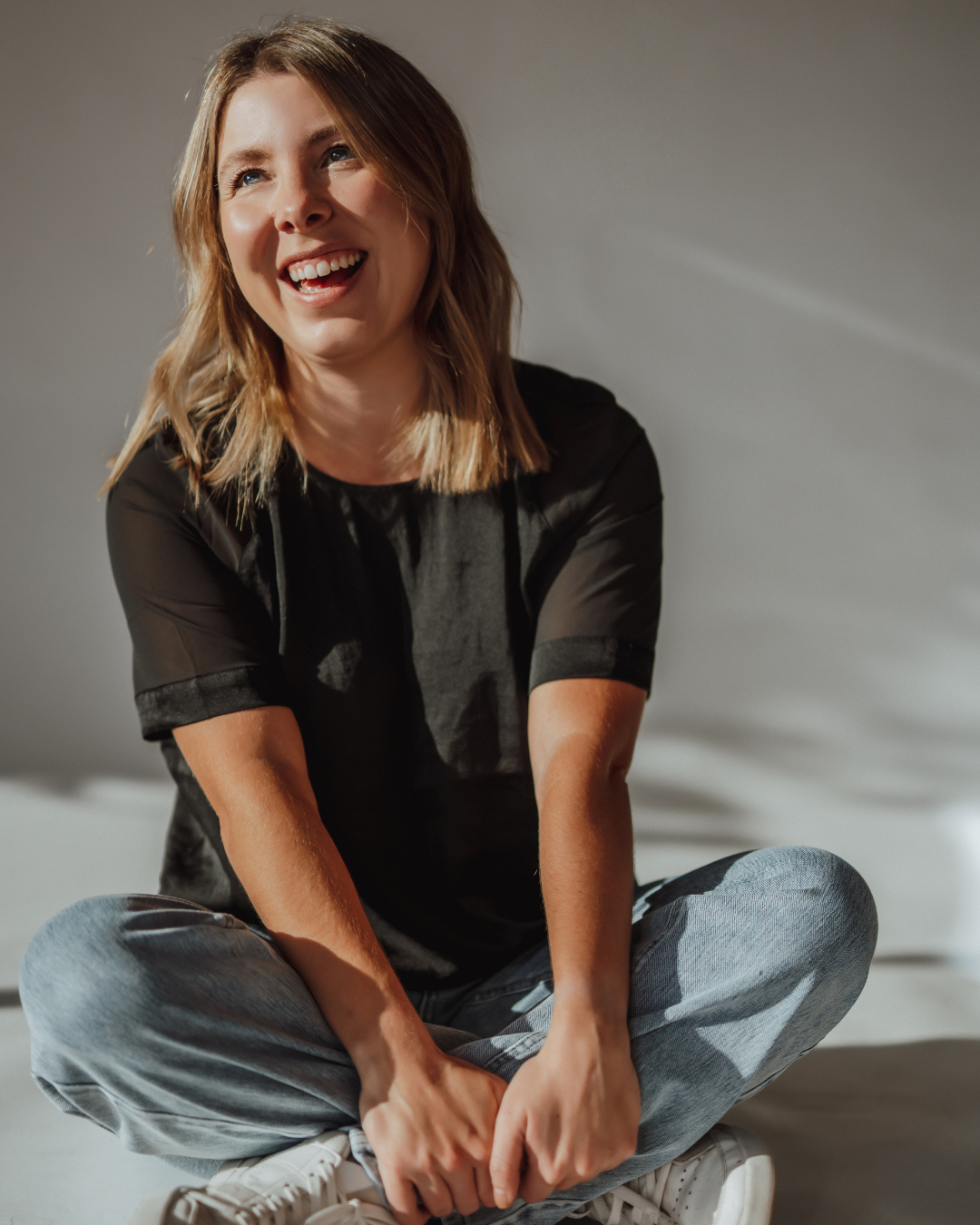 Smiling woman with blond hair in a salon, wearing a white shirt and jeans.