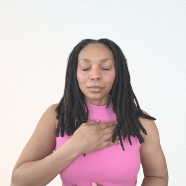 Woman with dreadlocks in a pink sleeveless top with eyes closed and hand over her chest, practicing mindfulness or meditation.
