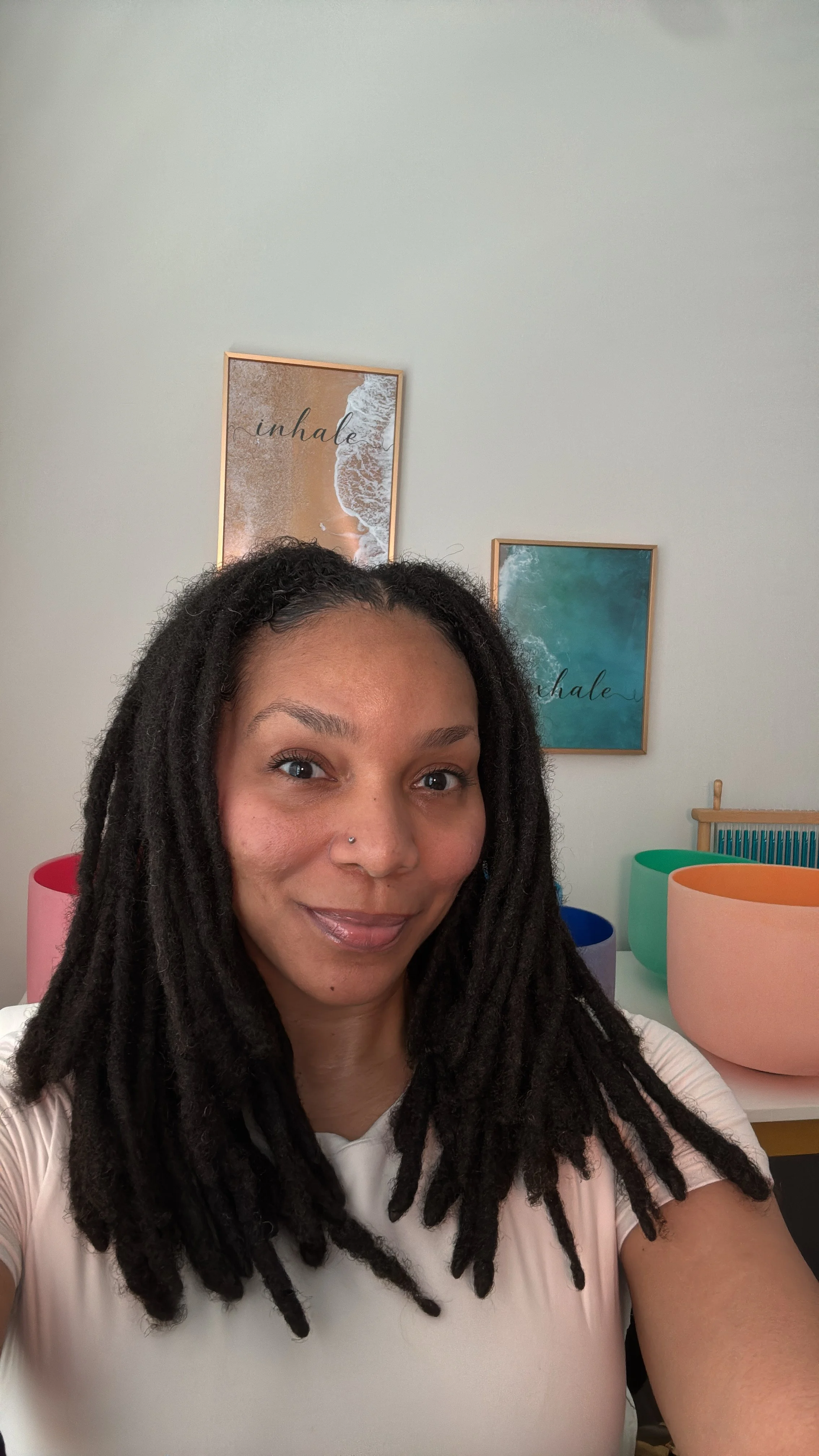 A woman with dreadlocks taking a selfie in a room with colorful bowls and wall art.