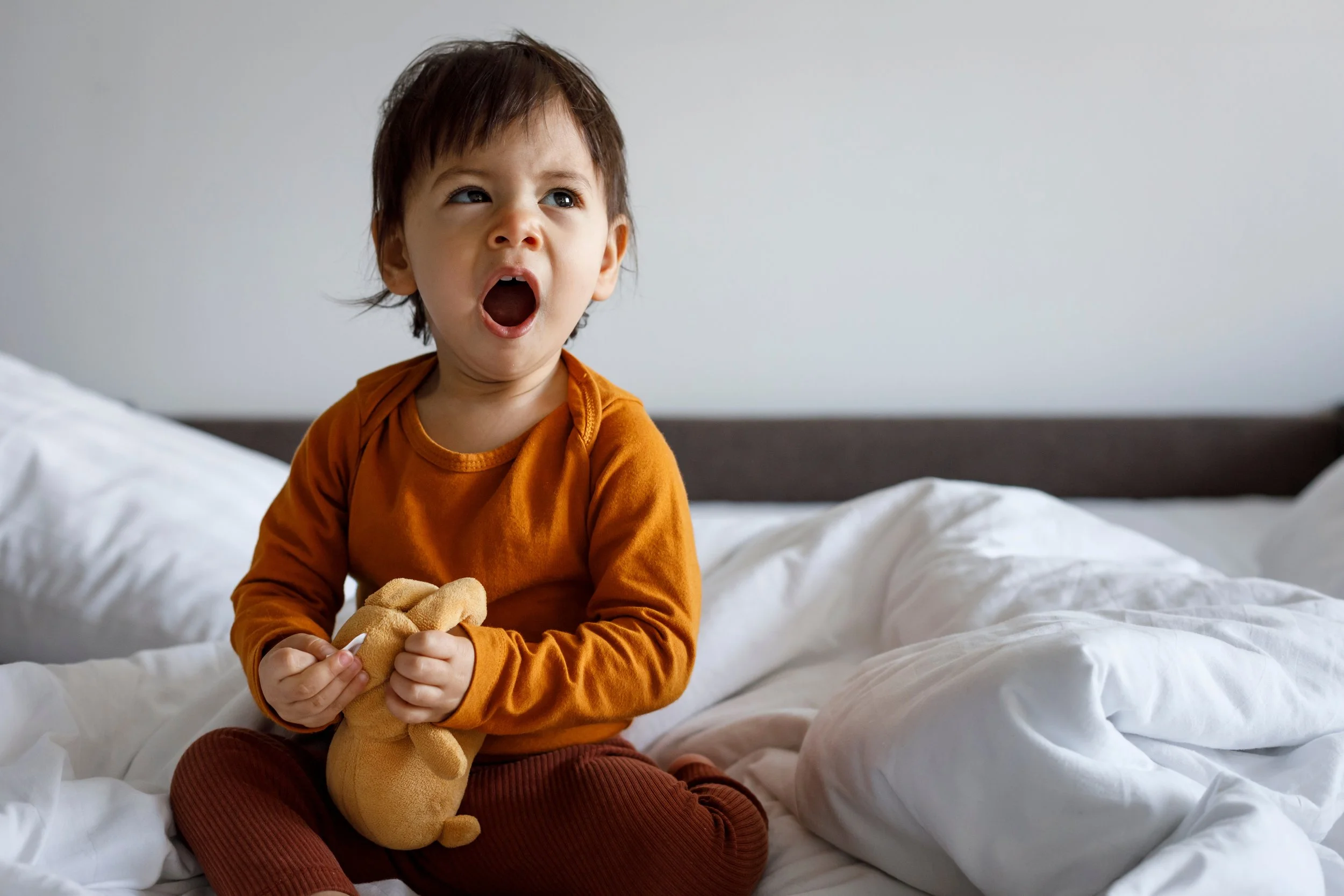 toddler yawning in bed and holding a stuffed animal