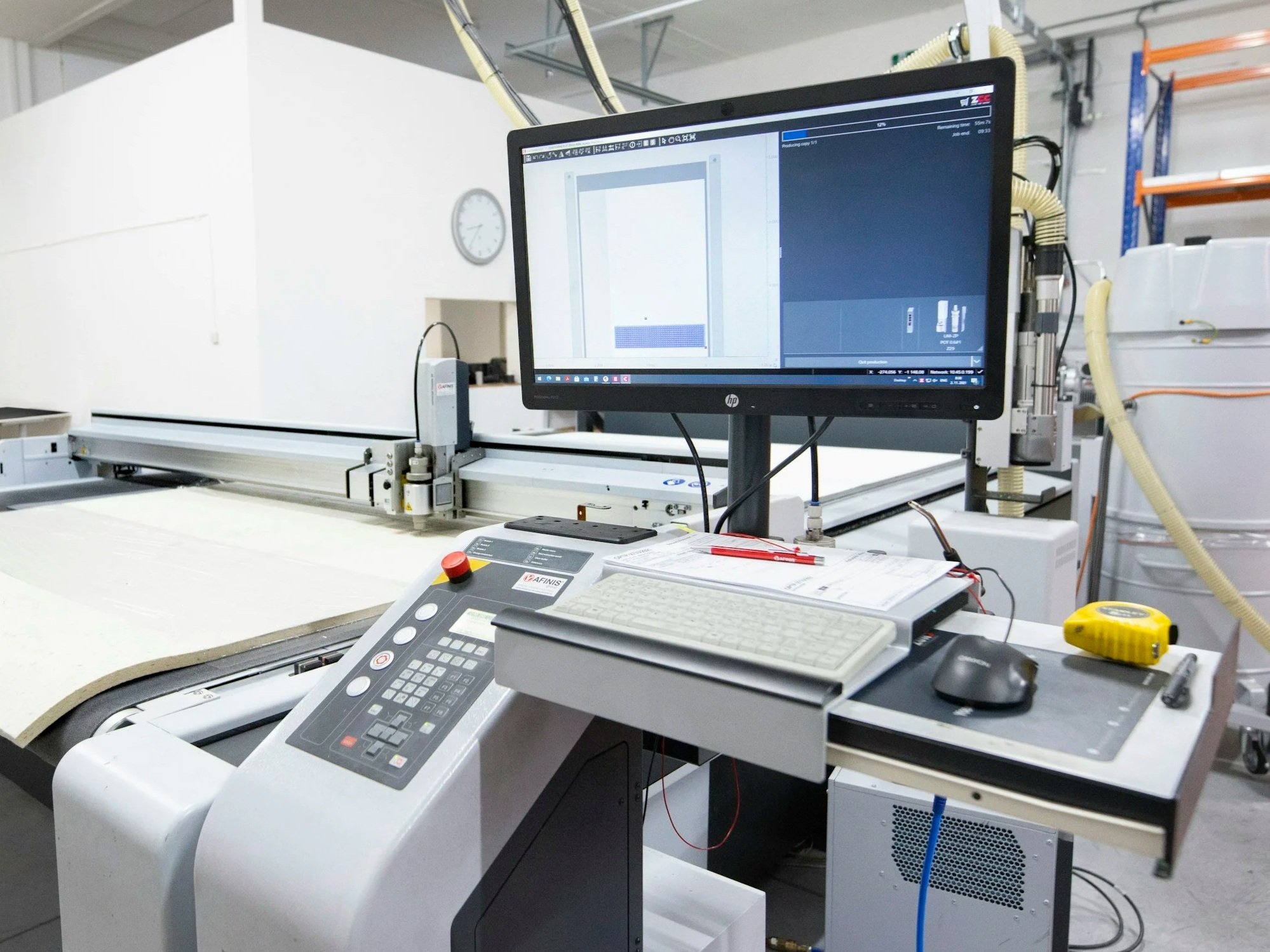 Machine de laboratoire avec un écran d'ordinateur, un clavier, une souris et divers dispositifs de commande sur une surface de travail blanche dans un environnement industriel.