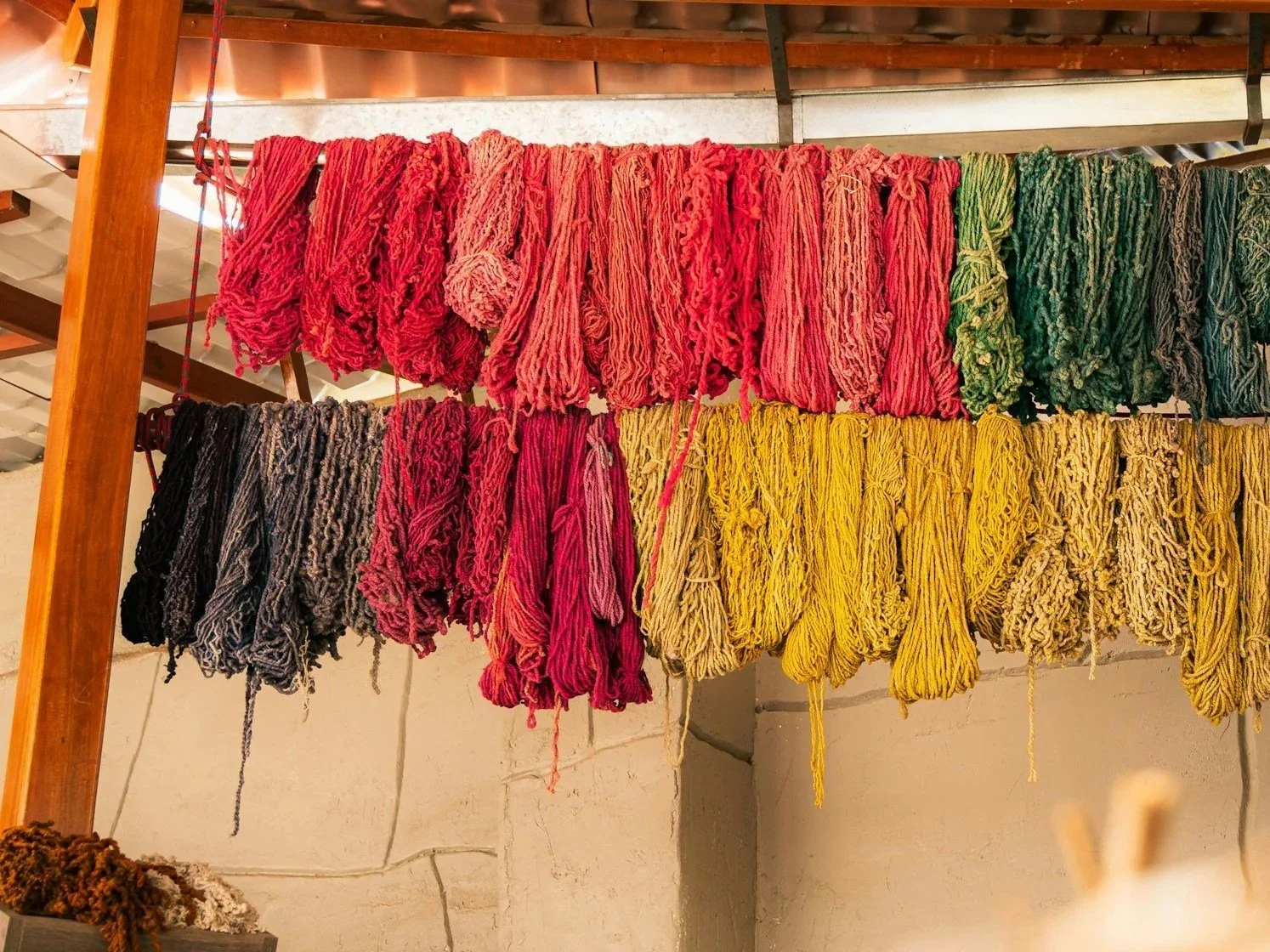 Des pelotes de laine colorées suspendues à un support en bois à l'intérieur.