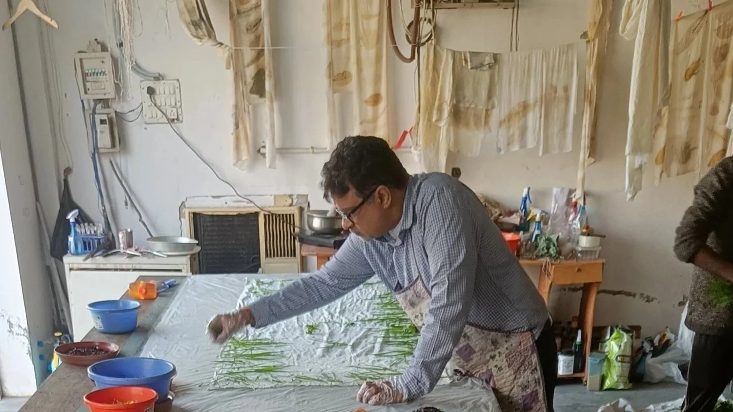 Personne portant un t-shirt blanc et un pantalon noir, avec une écharpe beige à motifs abstraits autour du cou.