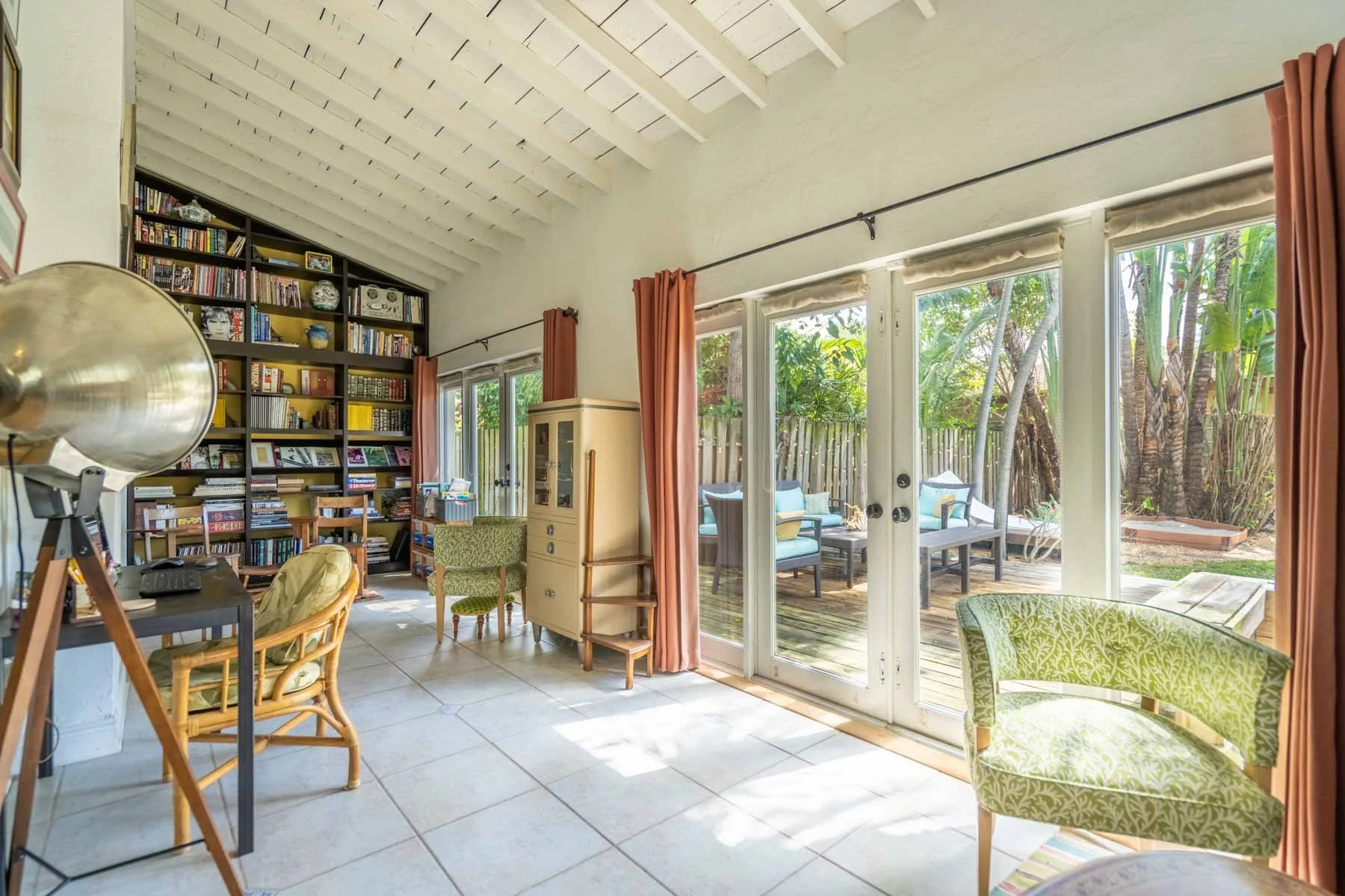 Living room with large sliding glass doors leading to an outdoor patio, house plants, a bookshelf, various chairs, and a telescope.