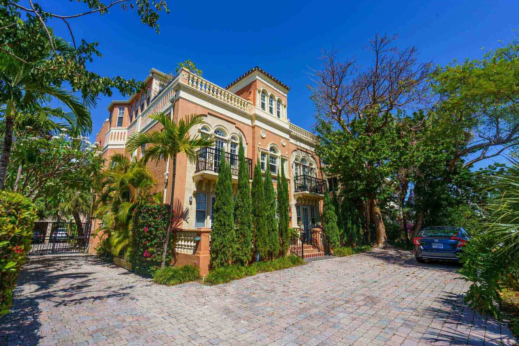 A large three-story house with a pinkish-orange facade and white decorative trim, surrounded by tall trees and lush greenery. The house features multiple arched windows, balconies with black railings, and a sloped roof with tiles. The driveway is cob