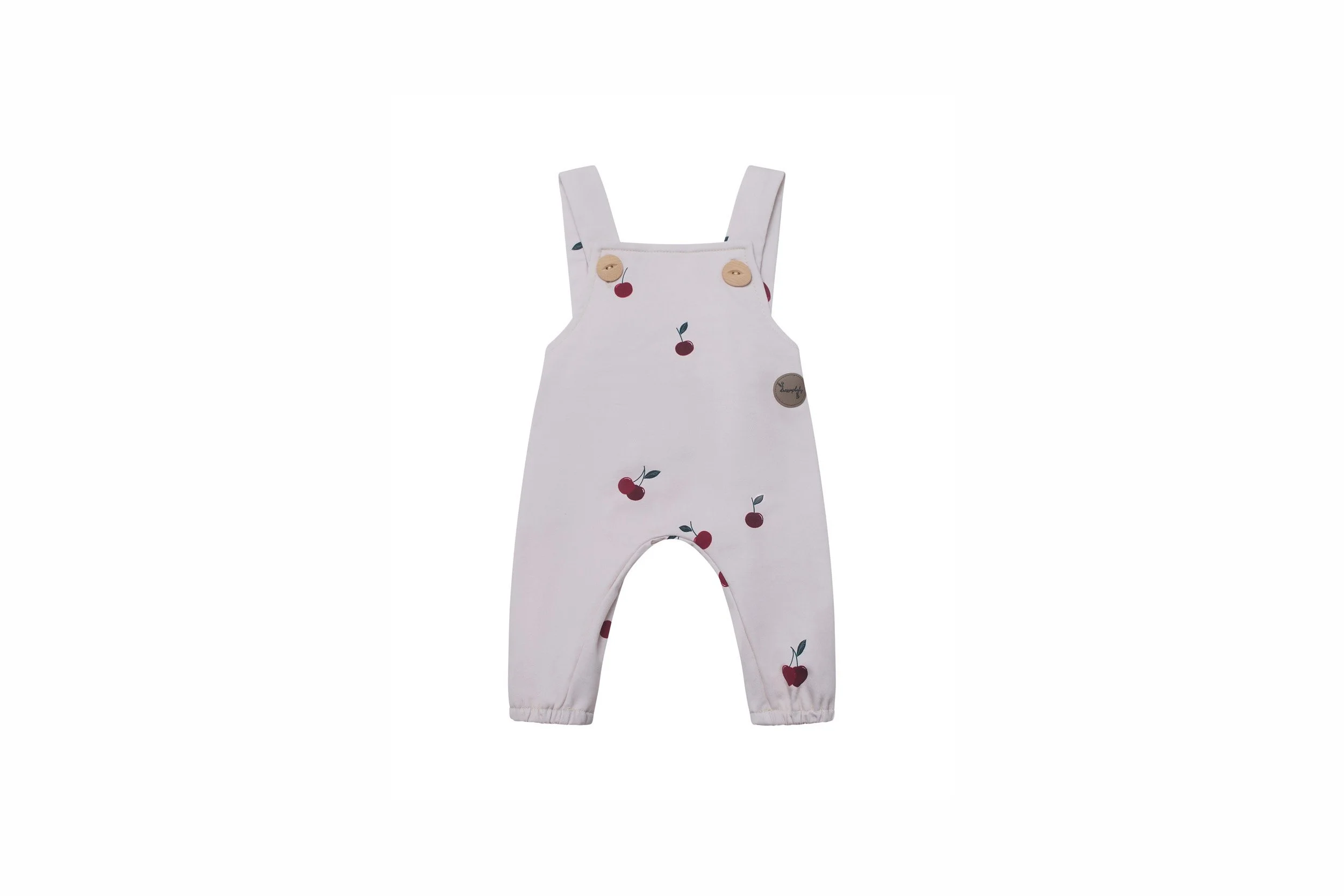 Cream-colored baby dungarees with red cherry print and wooden button straps on a white background