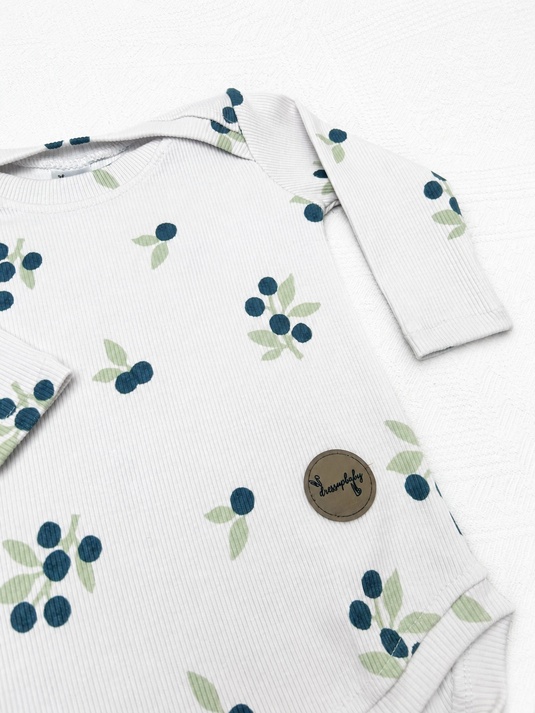Close-up of the Blueberry Baby Bodysuit showing the blueberry print, ribbed cotton texture and DressUpBaby logo.