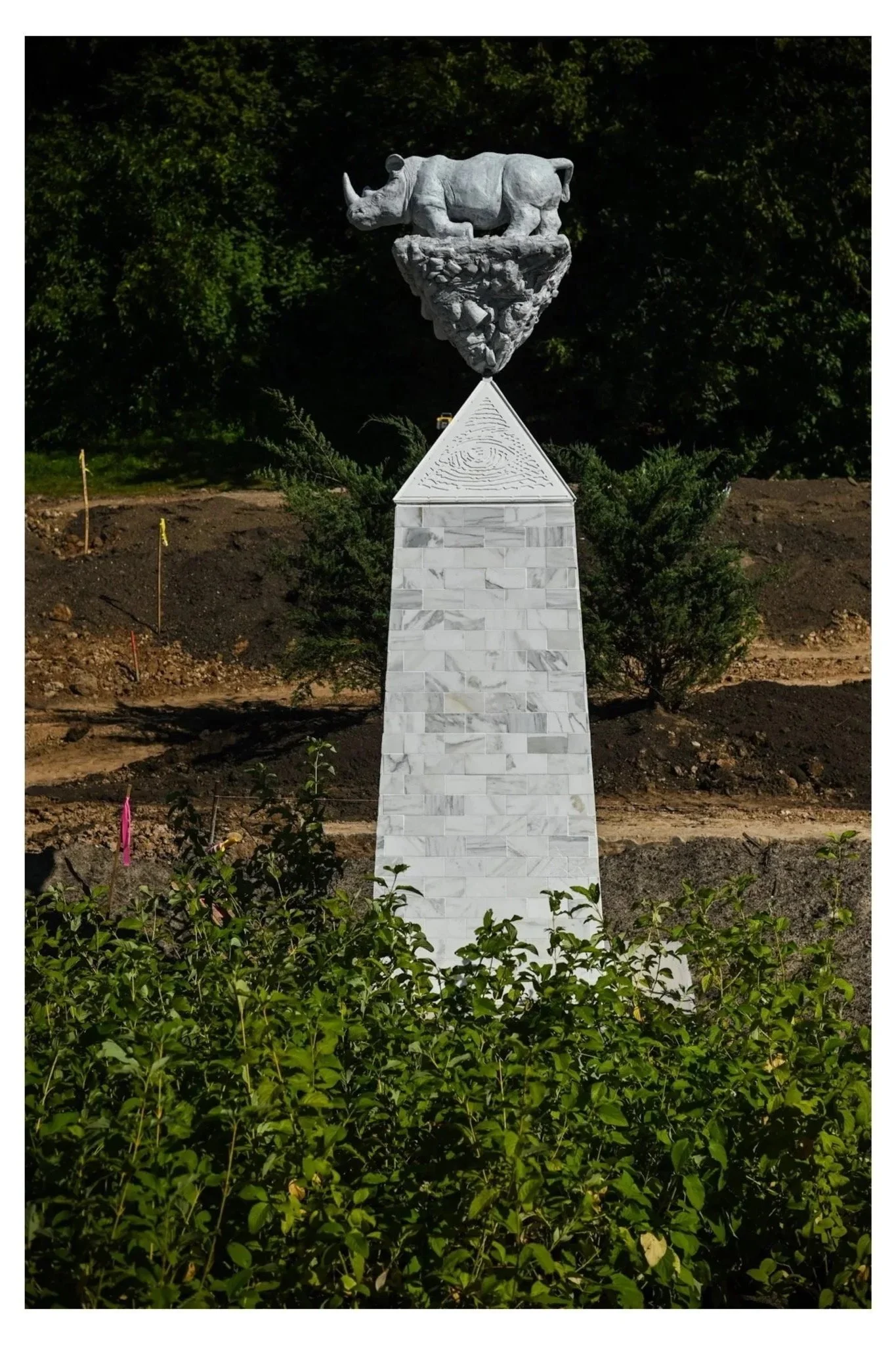 Outdoor Sculpture of northern white rhino on a l white marble obelisk with an inverted pyramid of sculpted wasteland
