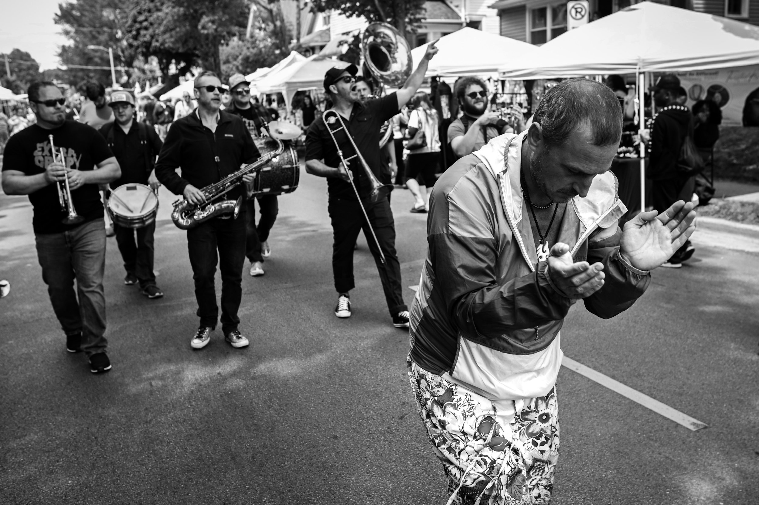 Street photo in black  and white of man dancing in front of a marching brass band in the streets of milwaukee  