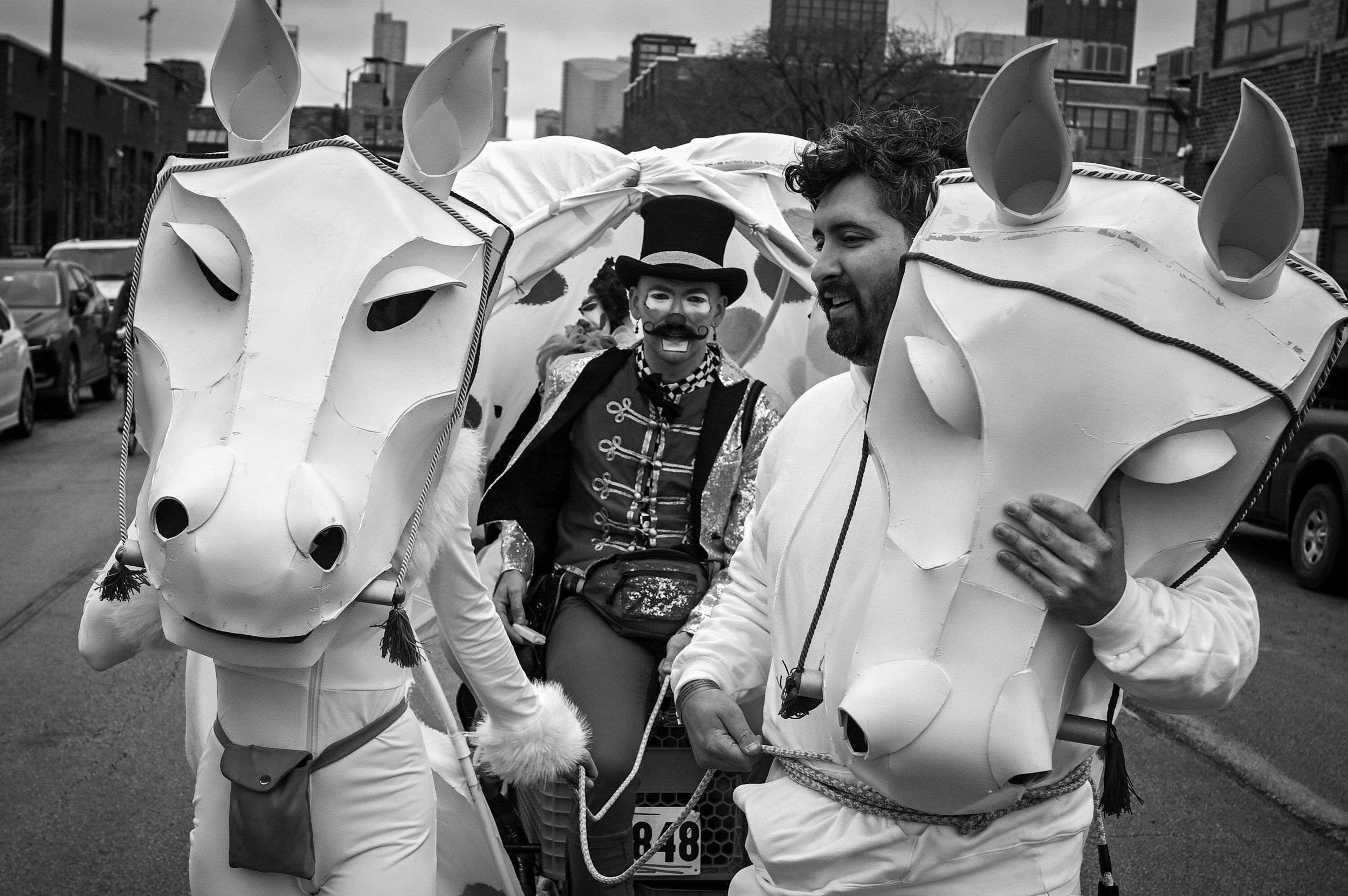 Two masked individuals with horse heads stand in front of a man that looks like a Ringmaster 