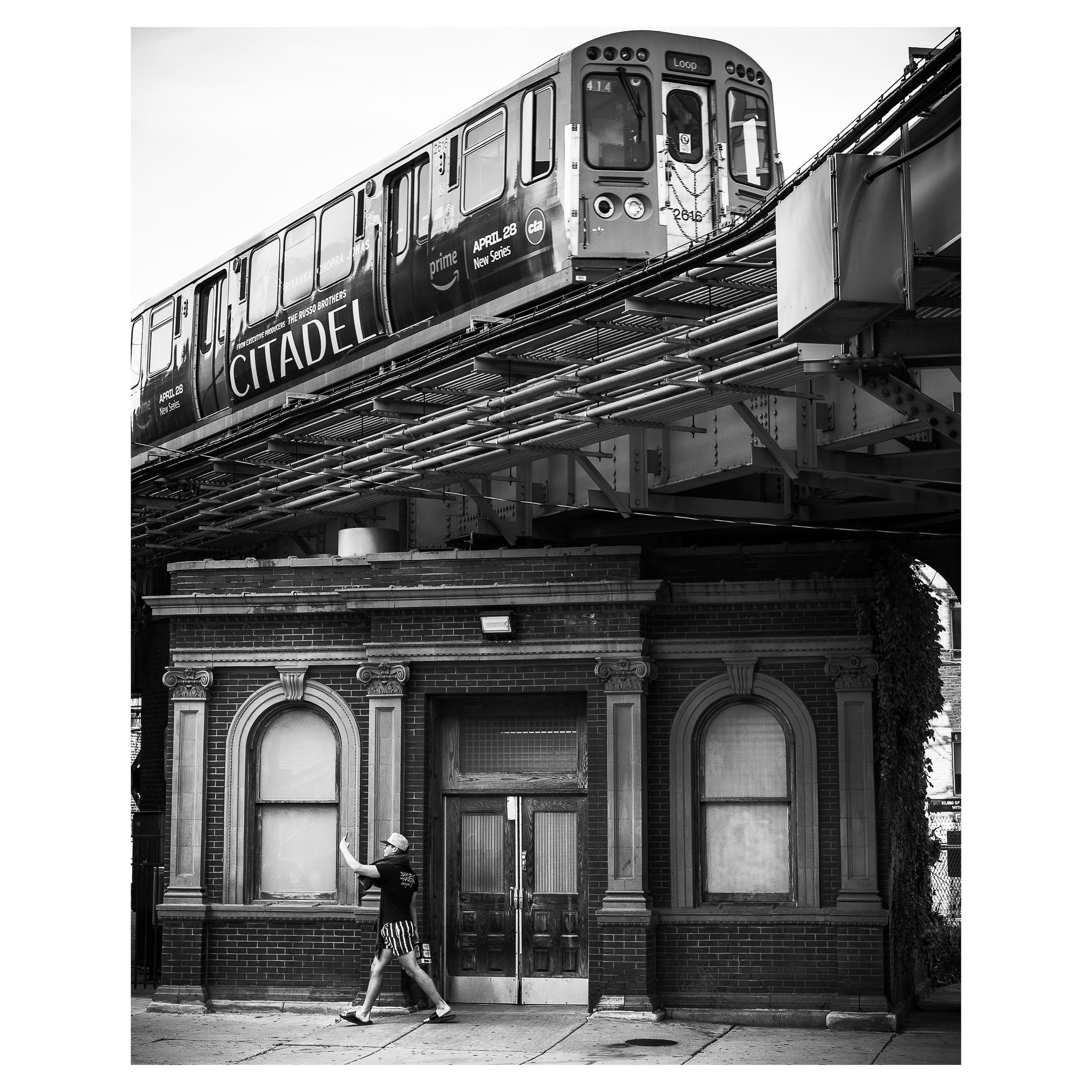Street Photo of the Chicago L train southbound with man in front of old train station taking a selfie.  