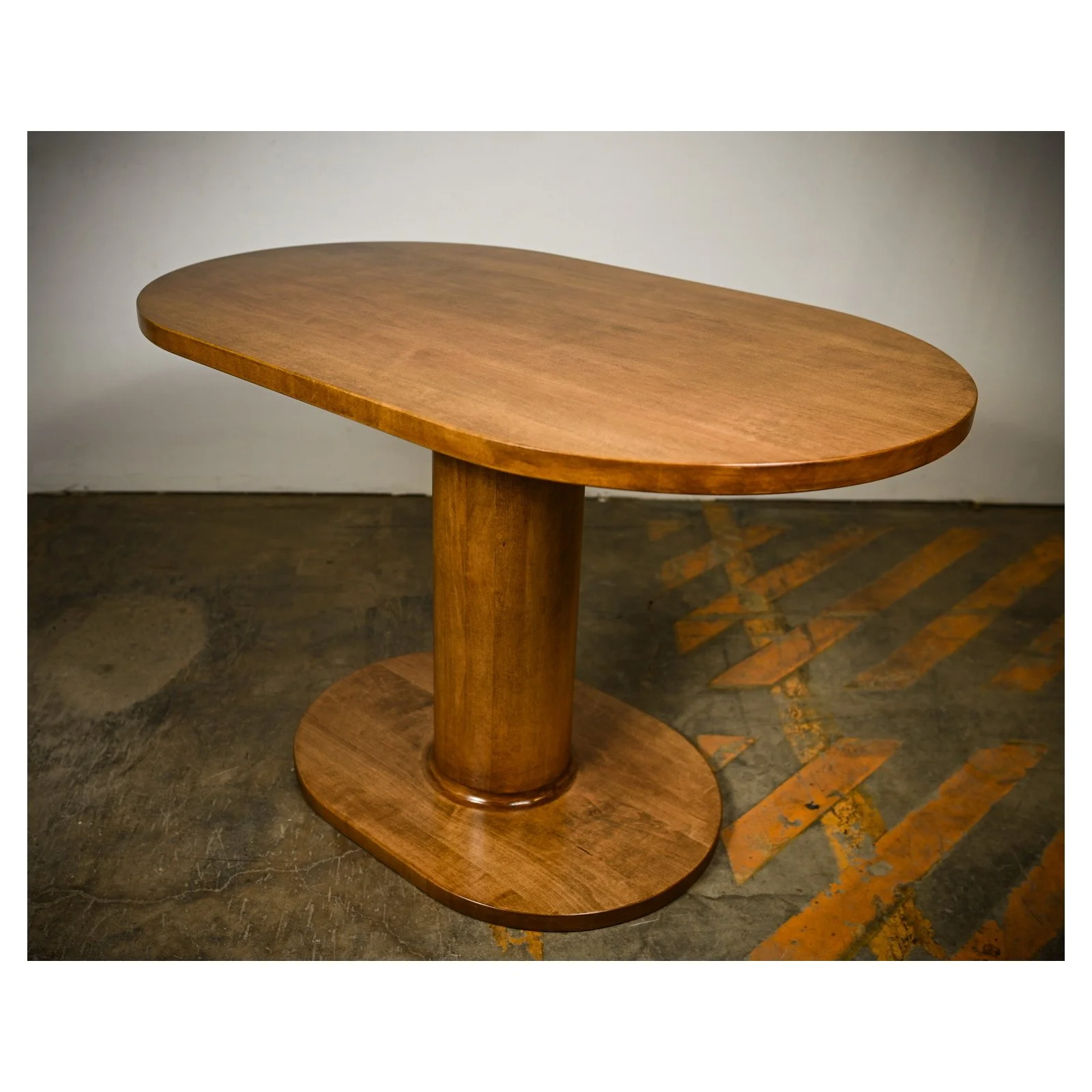 Solid maple dining nook table with cylindrical base and oval shaped top and footprint.   Modern design with natural wood tone finish.