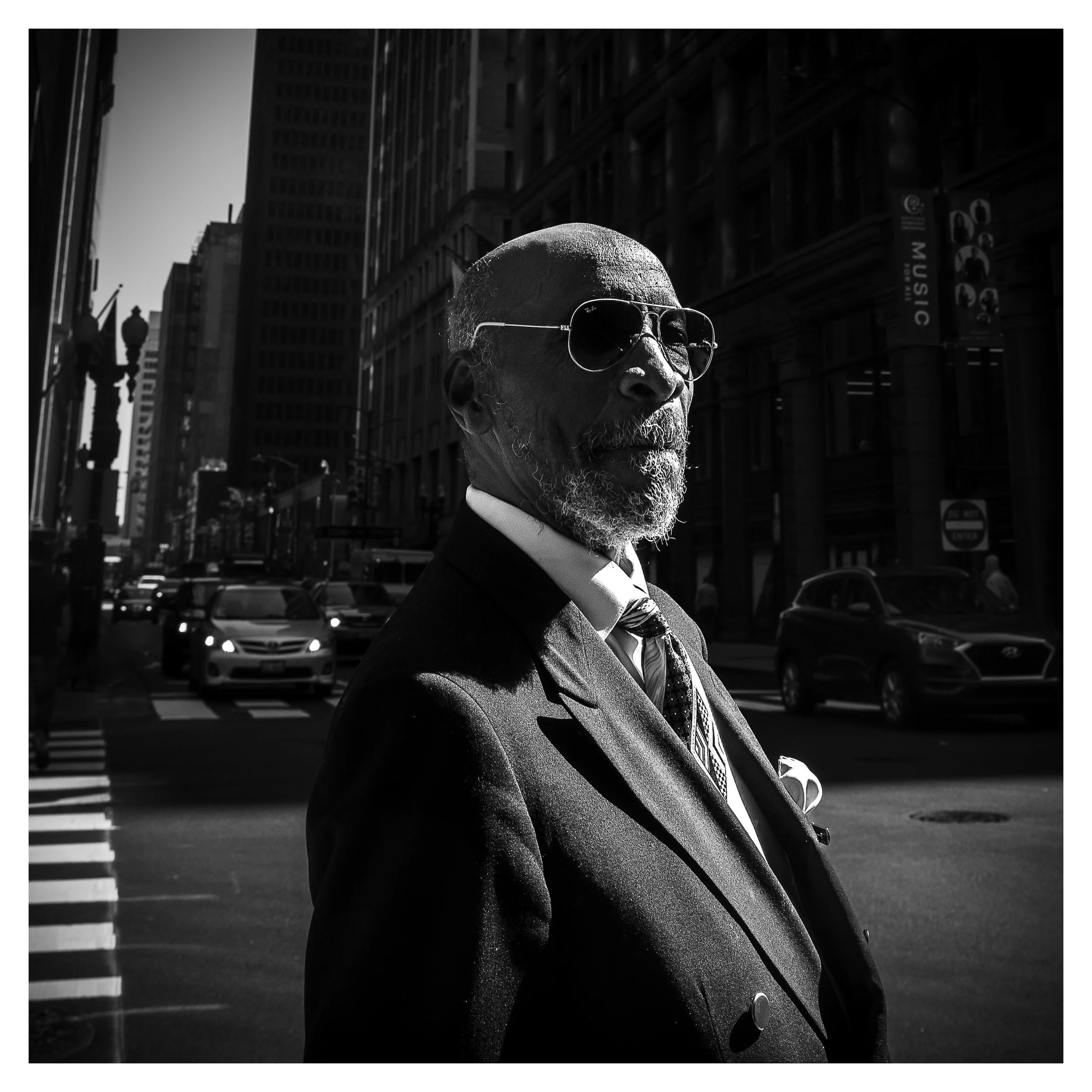 Candid street portrait of older black male in suit with strong chiarascuro lighting