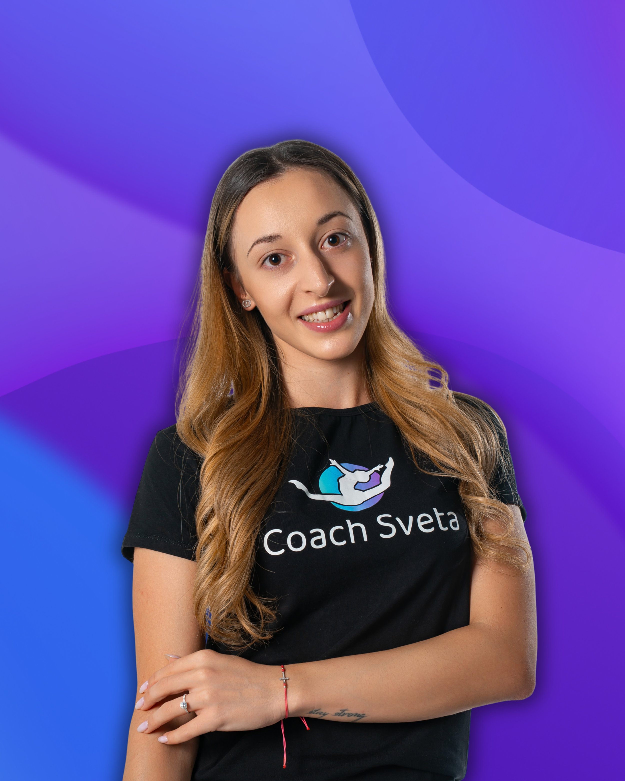 Smiling young woman with long wavy hair wearing a black t-shirt with a logo, standing against a purple gradient background.