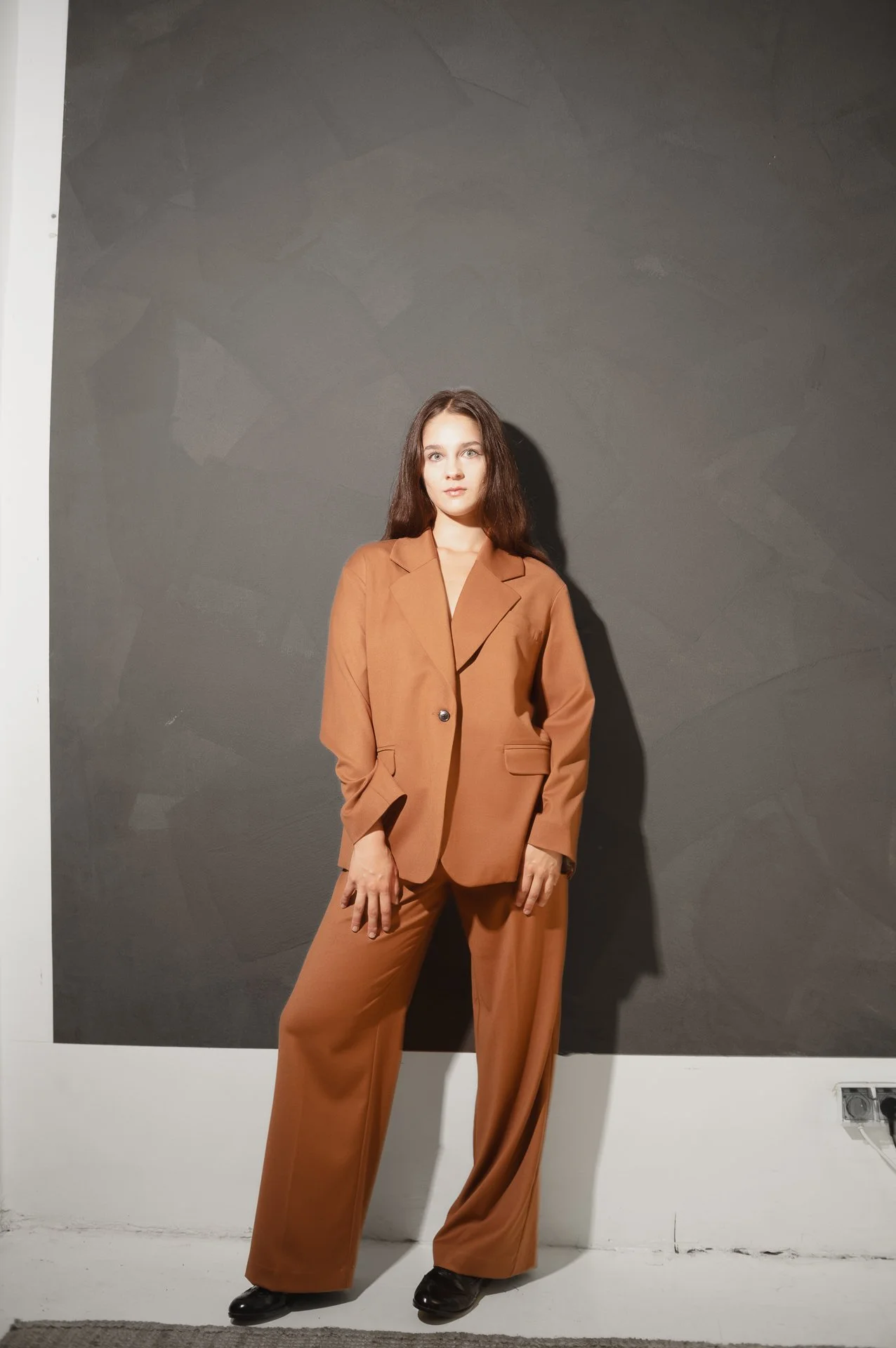 Woman in brown suit standing against a dark gray wall