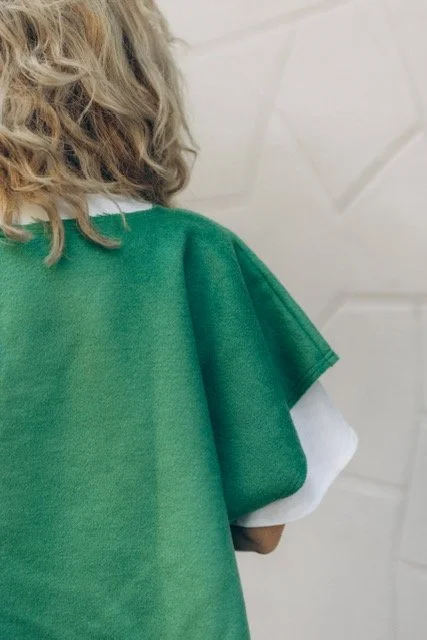 Back view of a person with curly blonde hair wearing a green and white shirt, standing against a textured wall.