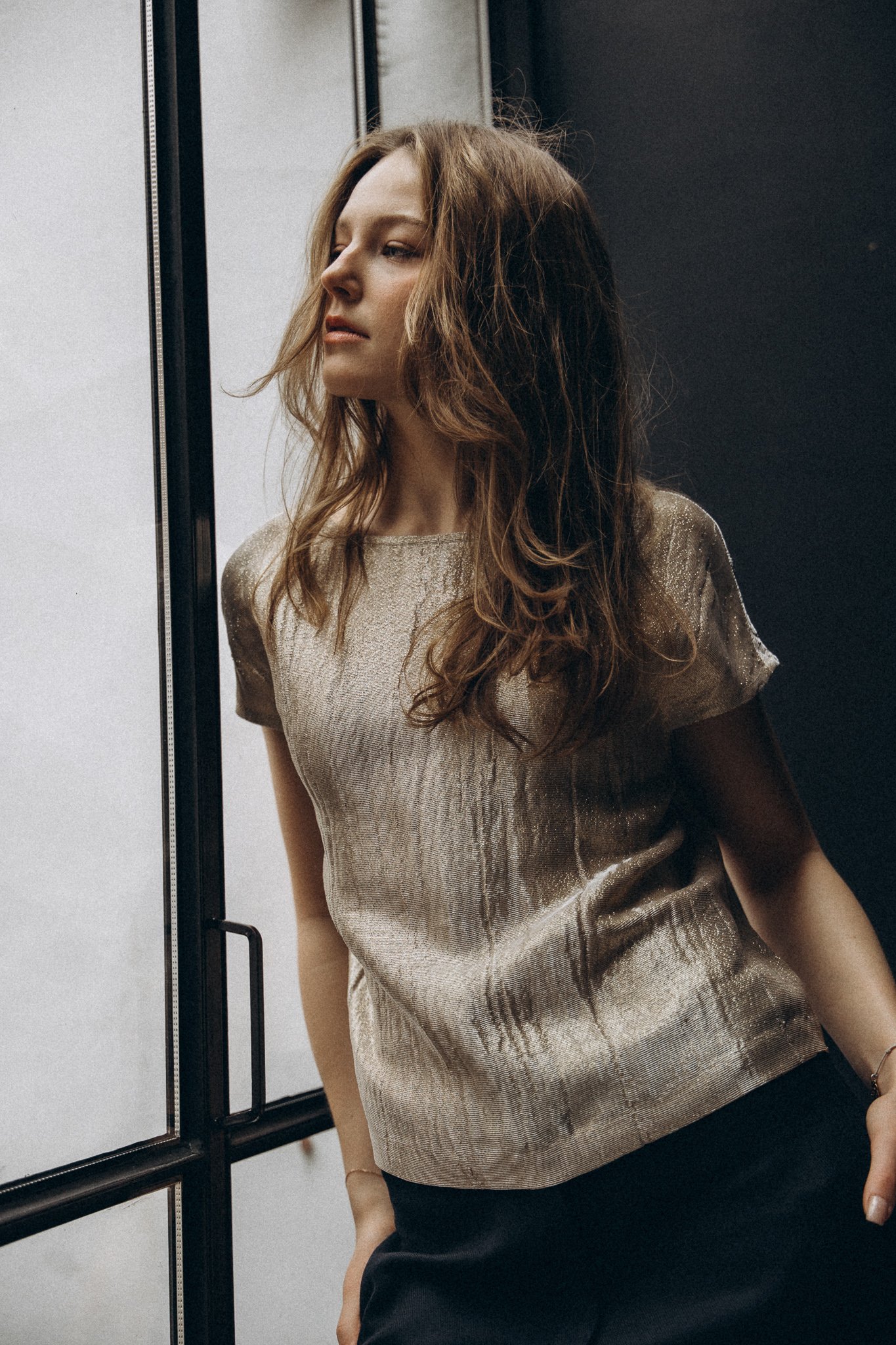 Woman in metallic top standing by window, looking outside