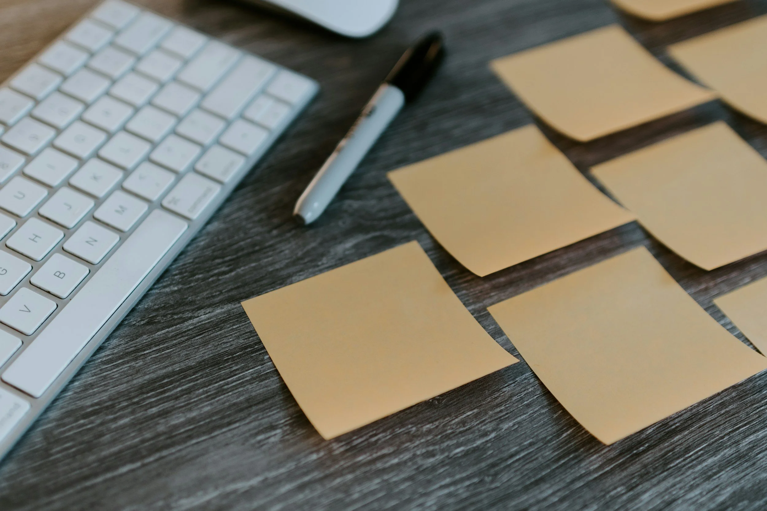 Computer keyboard, sticky notes, and marker on wooden desk
