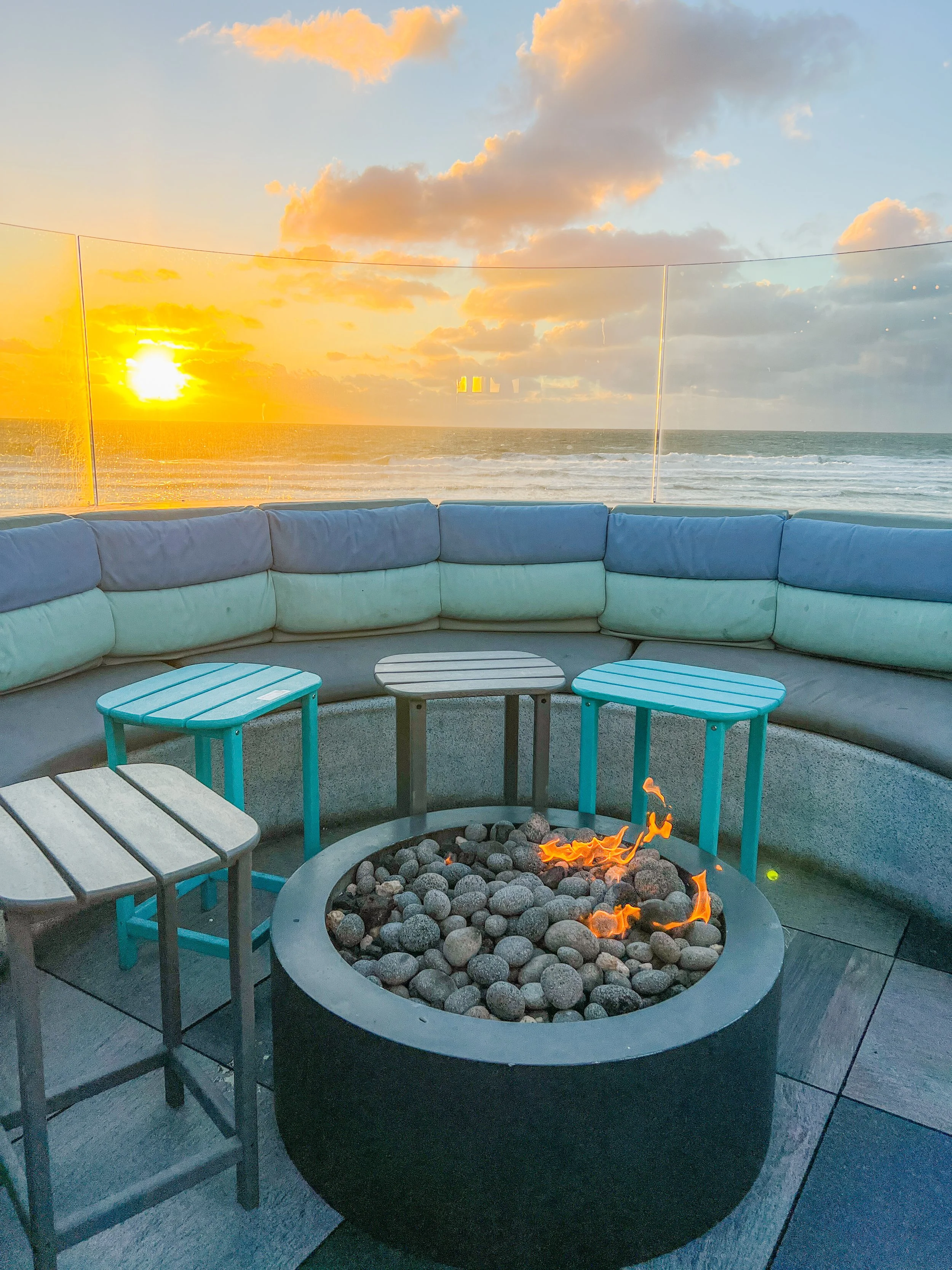 Outdoor fire pit with surrounding seating and a view of the ocean at sunset.
