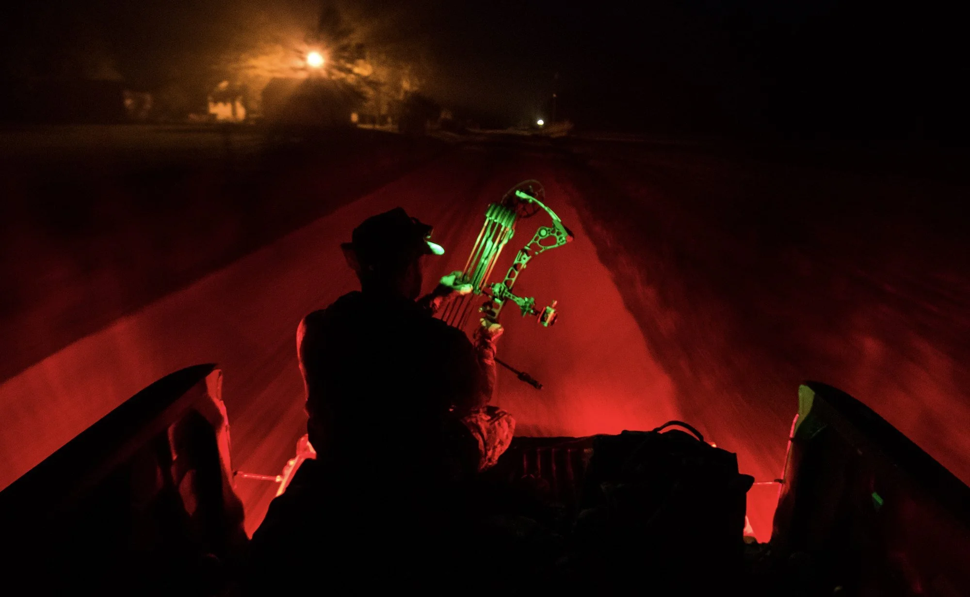 Bowhunter sitting in a truck bed under red light after dark, heading out from the hunt