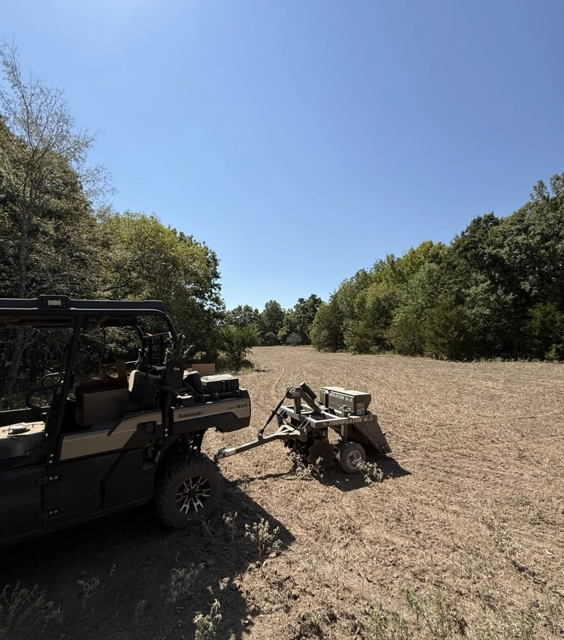 UTV pulling a seed drill across a freshly worked food plot along the timber edge
