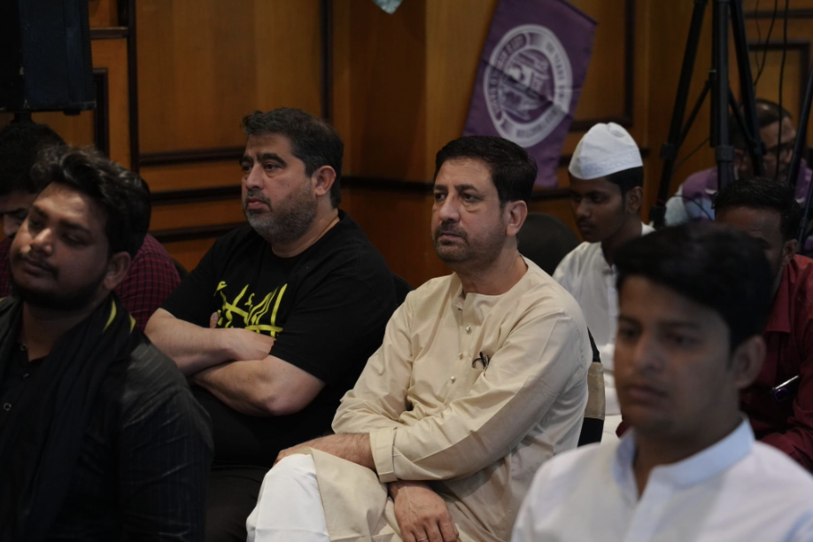 Dignitaries & participants seated on black chairs listening with rapt attention.