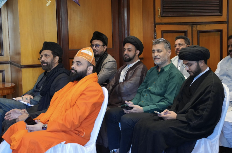 Dignitaries & participants seated on black chairs listening with rapt attention.