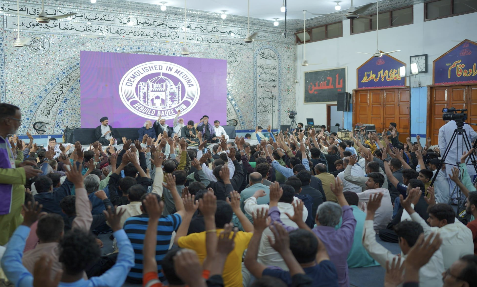 A nighttime gathering with an LED screen displaying Baqee visuals