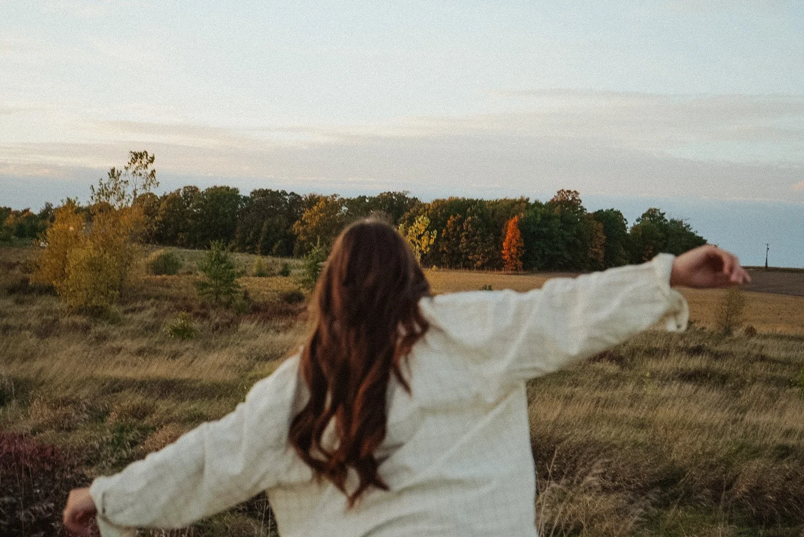 Woman standing in an open field with arms outstretched, facing away from the camera, symbolizing freedom and the perimenopause identity shift