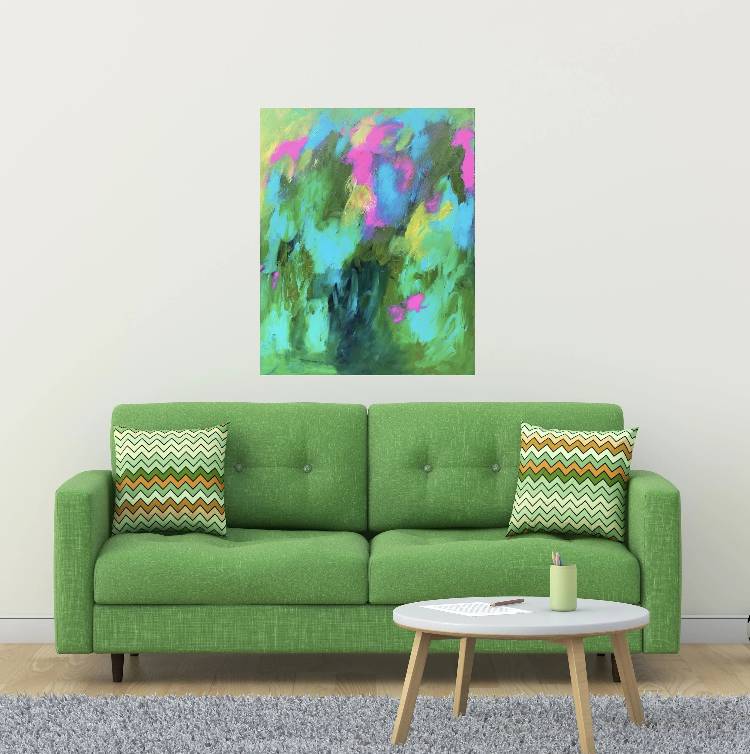 A bright green sofa with patterned throw pillows in front of a white wall, with an abstract colorful painting above it and a small round coffee table with a notepad, pen, and a small container holding pencils in front.