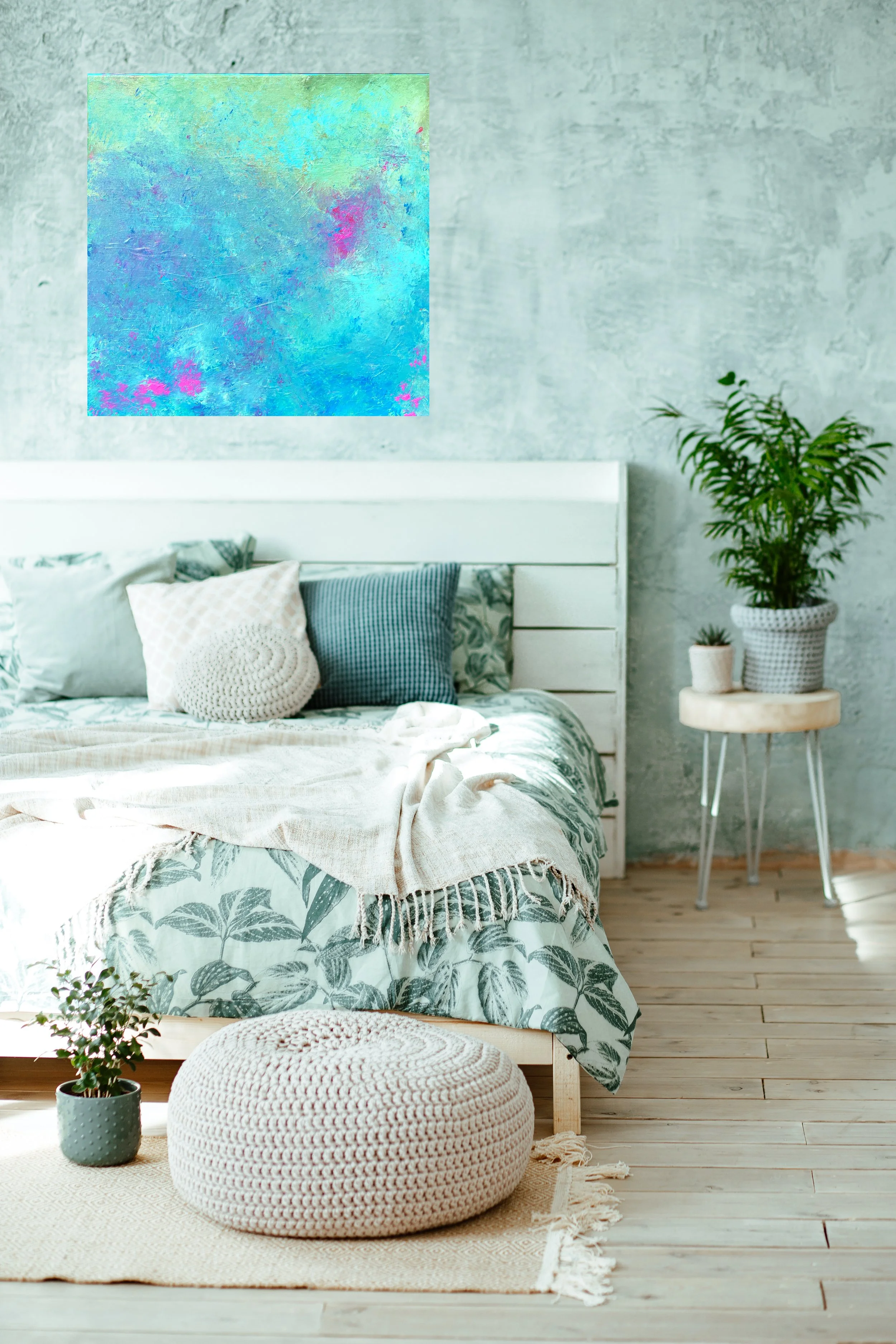 A cozy bedroom with a bed covered in patterned bedding, pillows, and a cream throw blanket. To the right of the bed, a small round table holds a potted plant. A larger potted plant is on the floor to the right. An abstract, colorful painting hangs ab