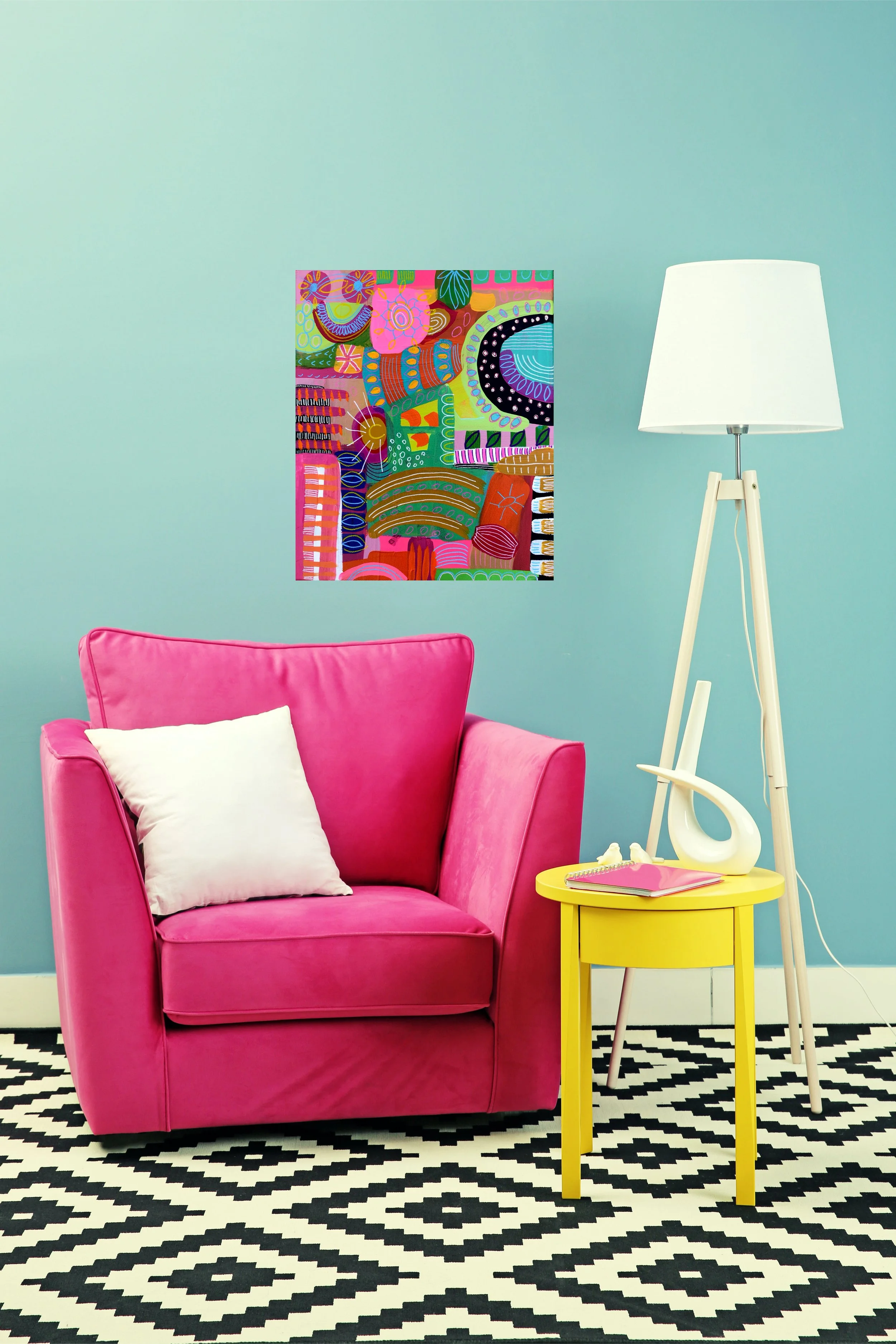 Interior room with a pink armchair, a white pillow, a yellow side table, a white reading lamp, and colorful abstract wall art on a blue wall, with a black and white patterned rug.