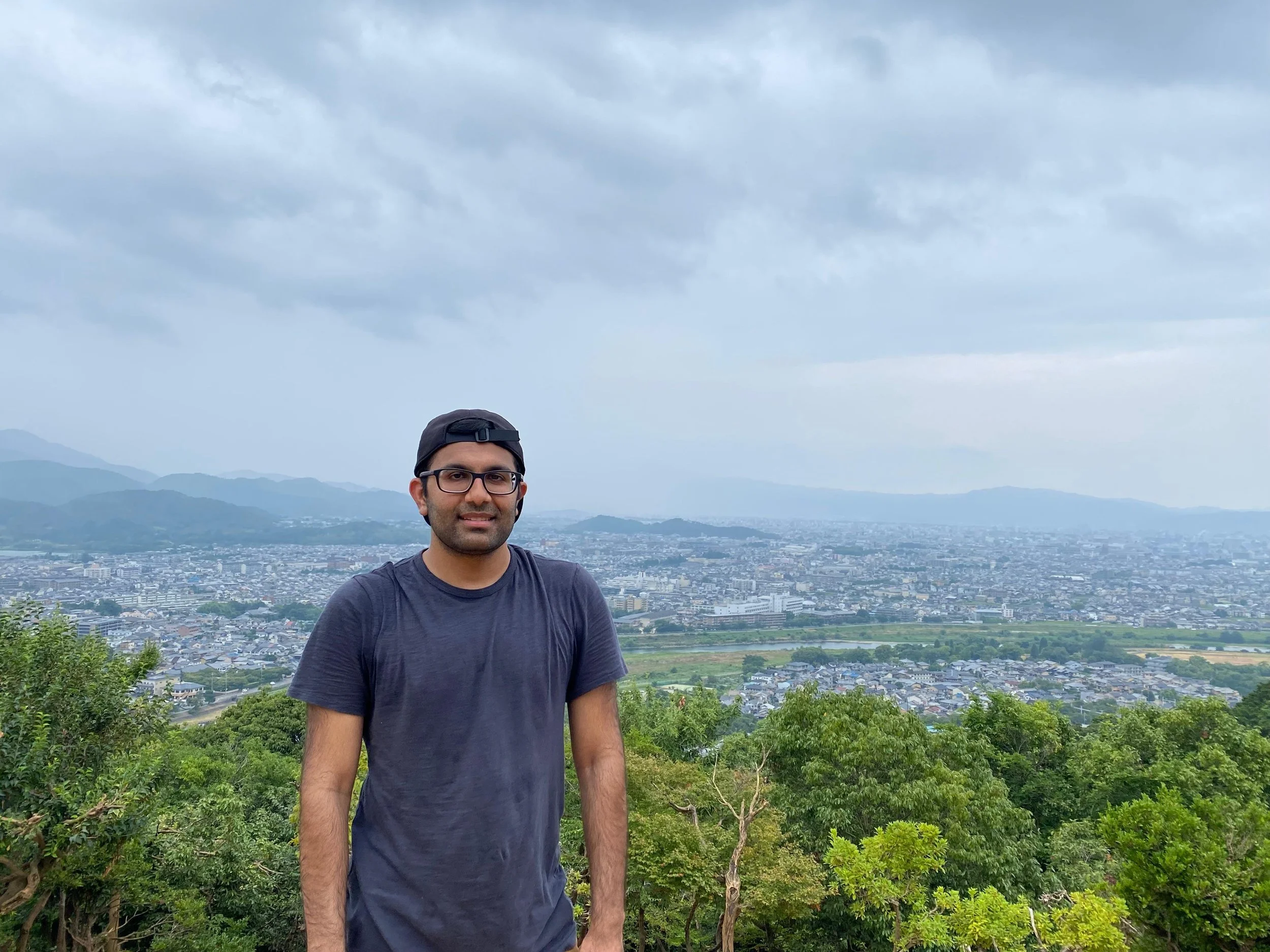 Man on top of a hill with view of city and mountains behind him