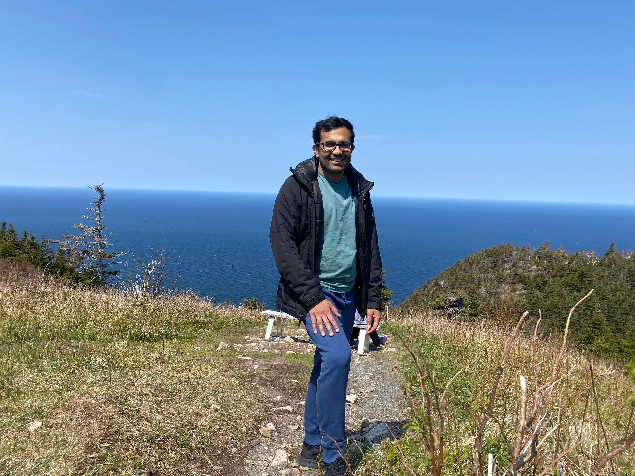 Man on hiking trail with view of water and sky behind him