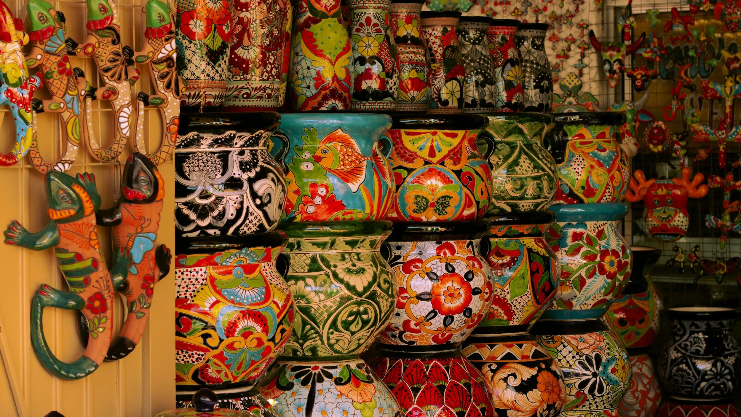 Colorful ceramic pottery and figurines with vibrant floral and butterfly patterns displayed on shelves at a store.