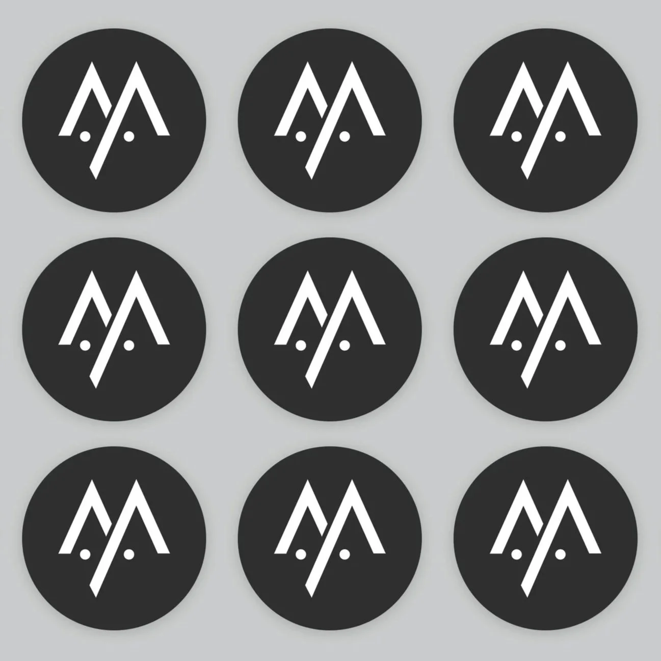 Six circular black stickers with white abstract logo resembling a stylized mountain and face, arranged in a 3x3 grid on a gray background.