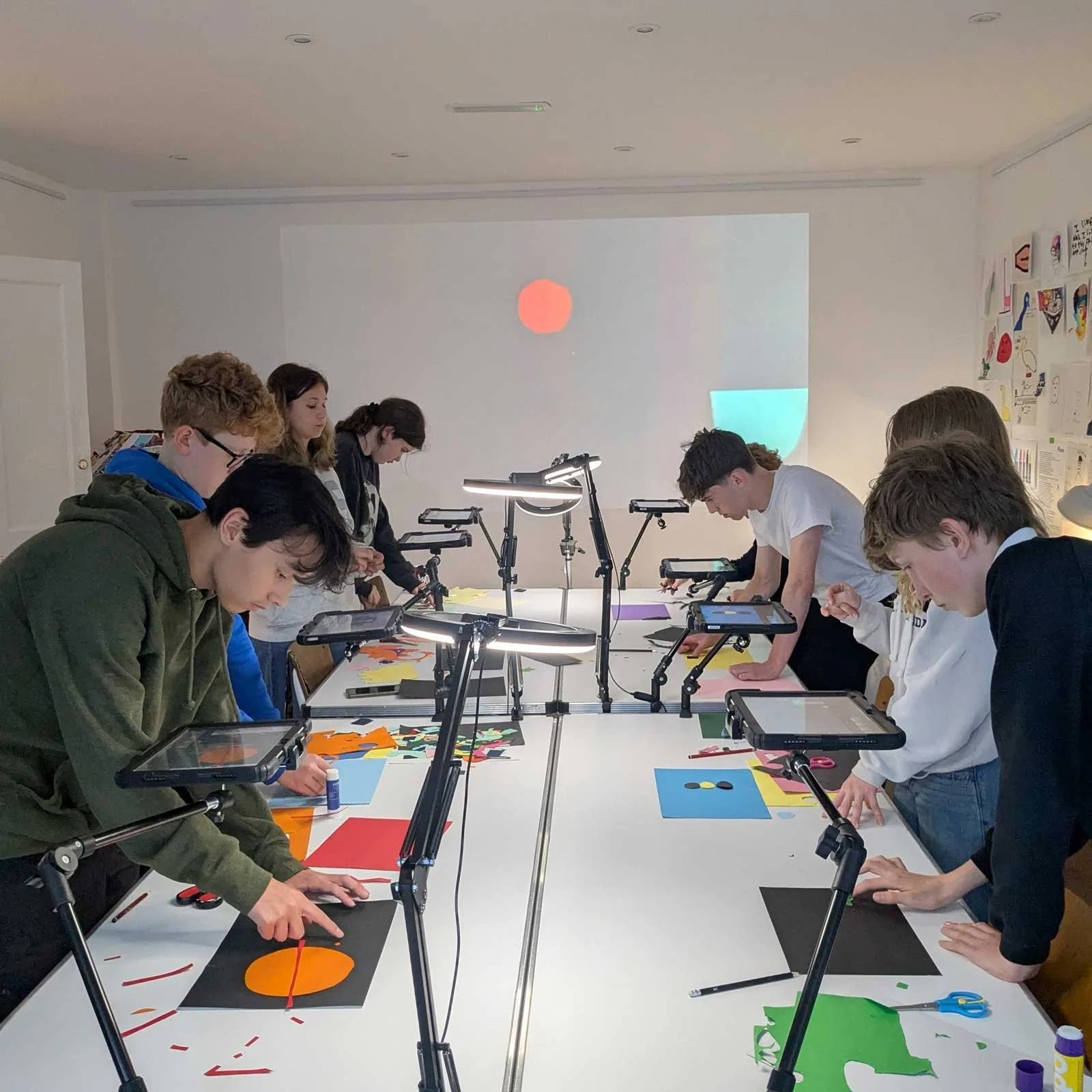 Group of students working on colorful paper art projects around a white table in a classroom setting at Submarine Art School, Edinburgh. Photo by Tom Ellis.