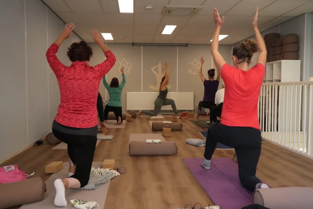 Kirsten Jense geeft yogales aan mensen met gekleurde tops in de practische yogastudio voor bedrijfsyoga in Puttershoek, Hoeksche Waard