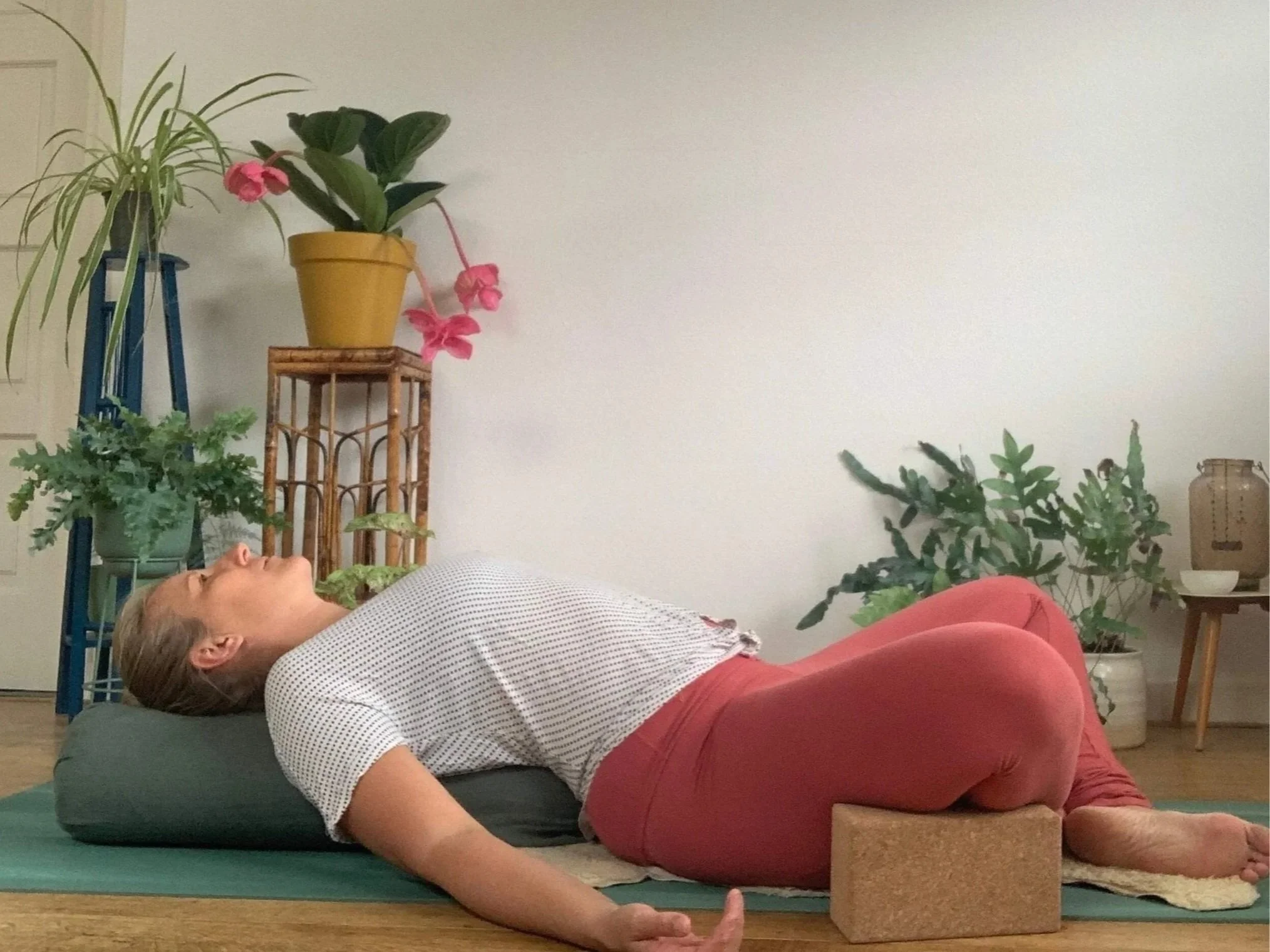 Kirsten Jense in roze legging en witte top ligt rustig in een liggende ondersteunde vlinder houding op een yogamat. relax en yoga nidra voor diepe ontspanning en herstel. 