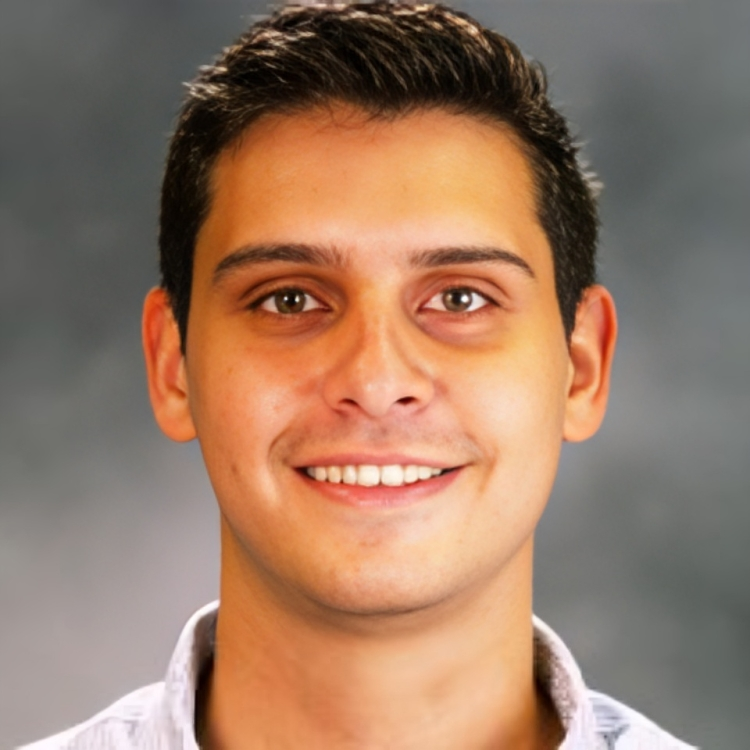 A portrait of a young man with short dark hair, smiling, against a blurred grey background.