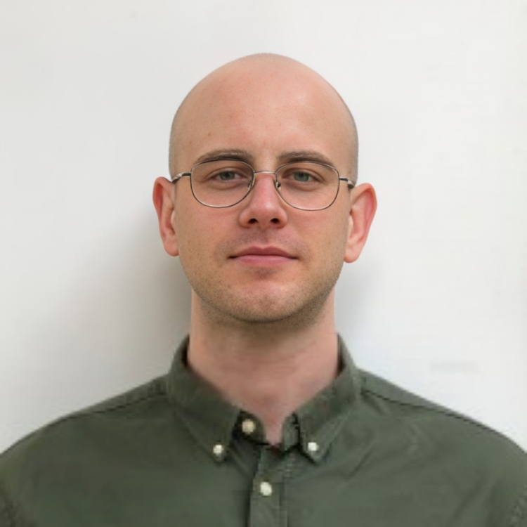 A bald man with glasses wearing a green button-up shirt against a plain white background.