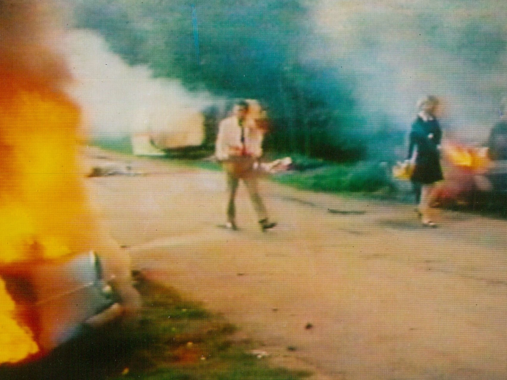 Three people walking away from a fire and smoke on the street with burning debris on the ground.