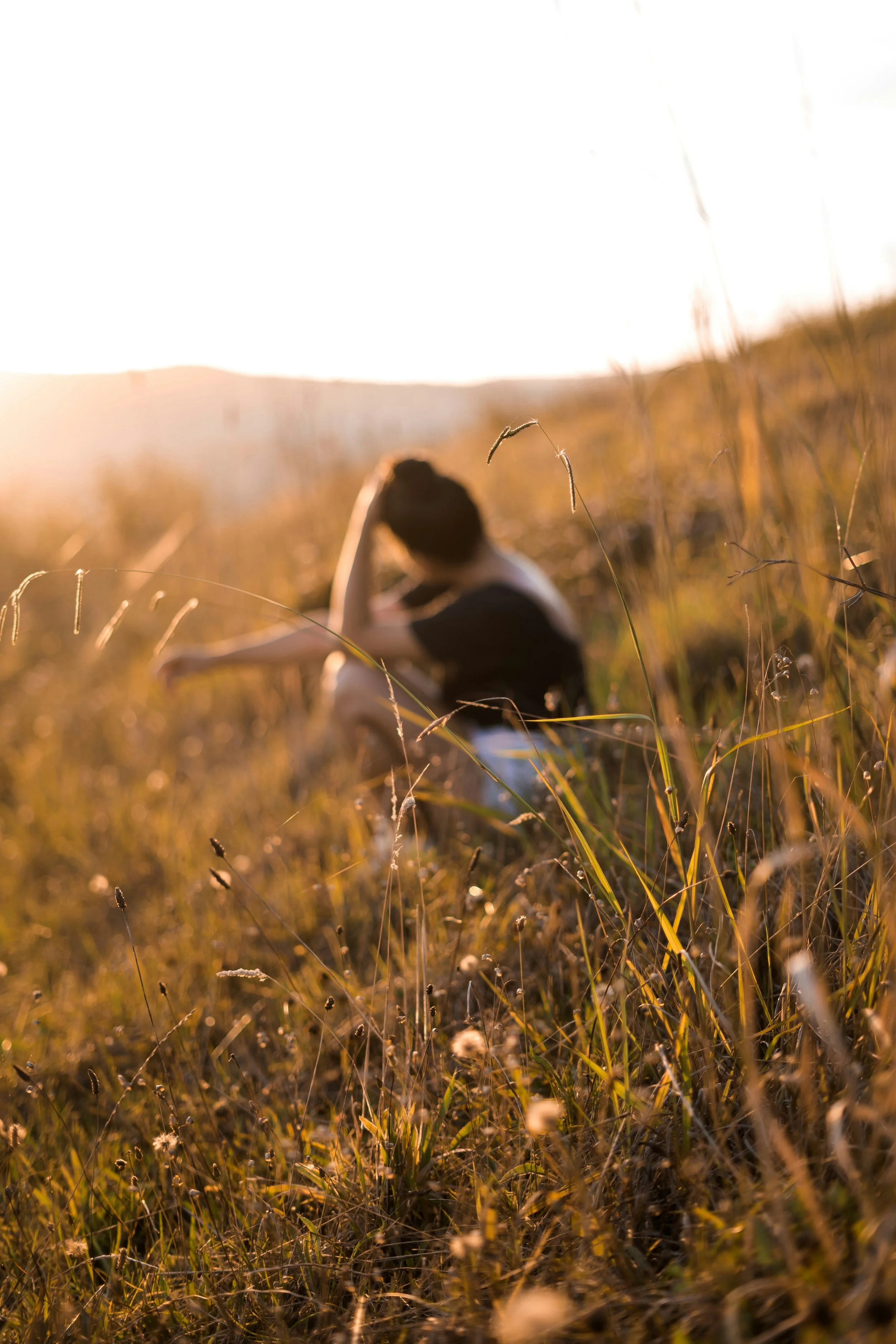 Blurred woman sits on a grassy hill symbolizing how it feels to be in the weeds of infertility