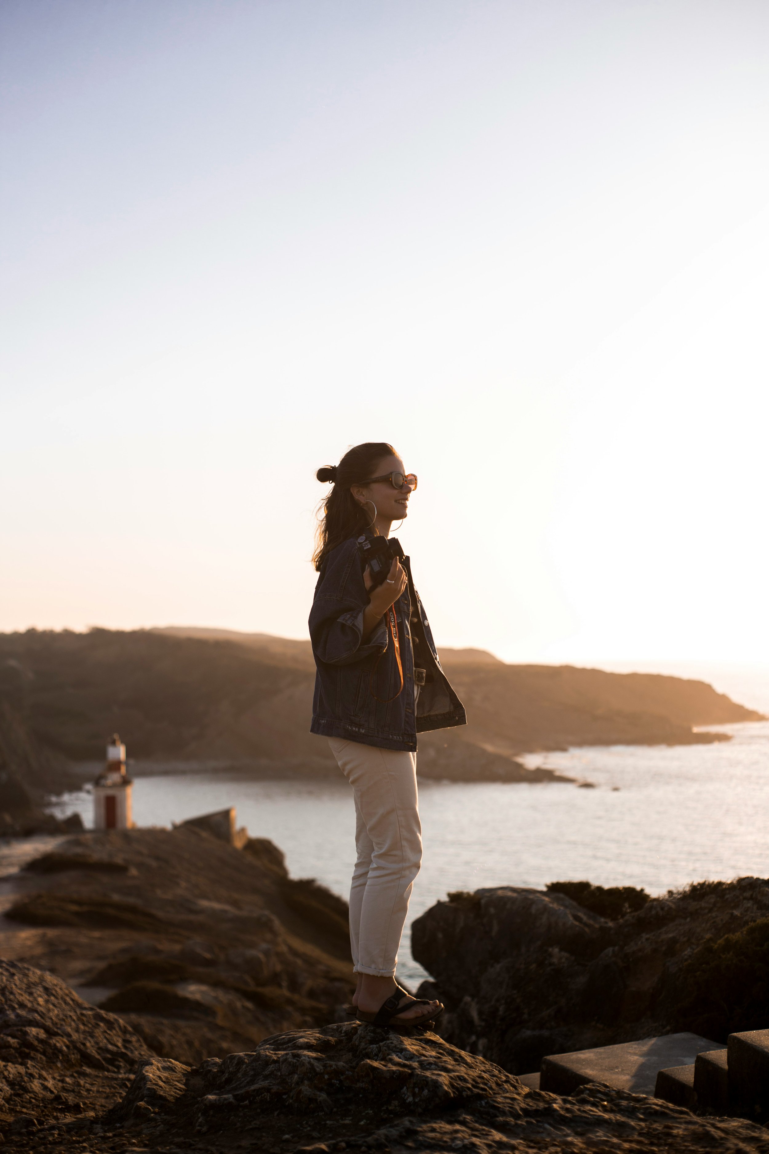 Smiling woman stands on a rocky coastline enjoying the early benefits of fertility acupuncture